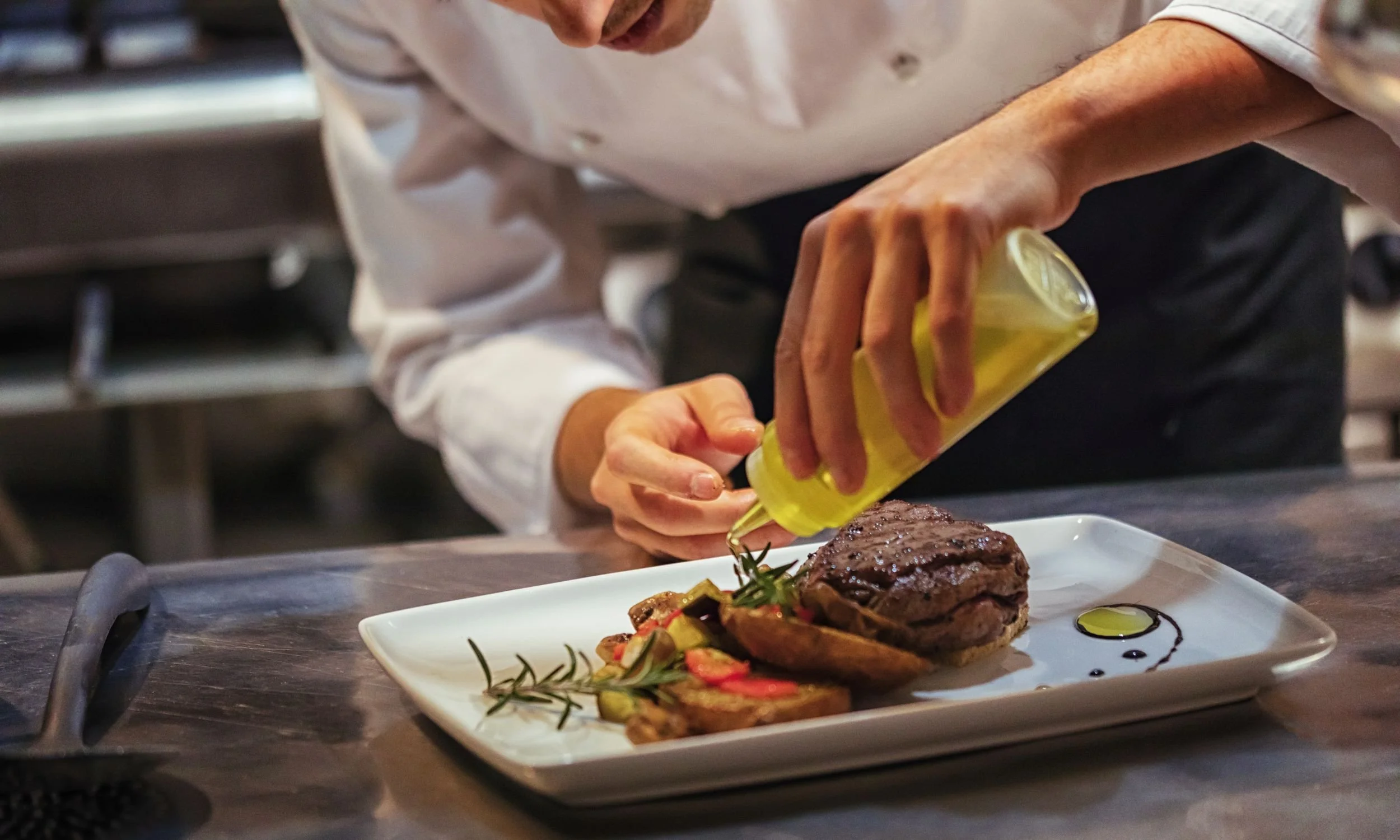 A chef drizzling oil on a gourmet hamburger.