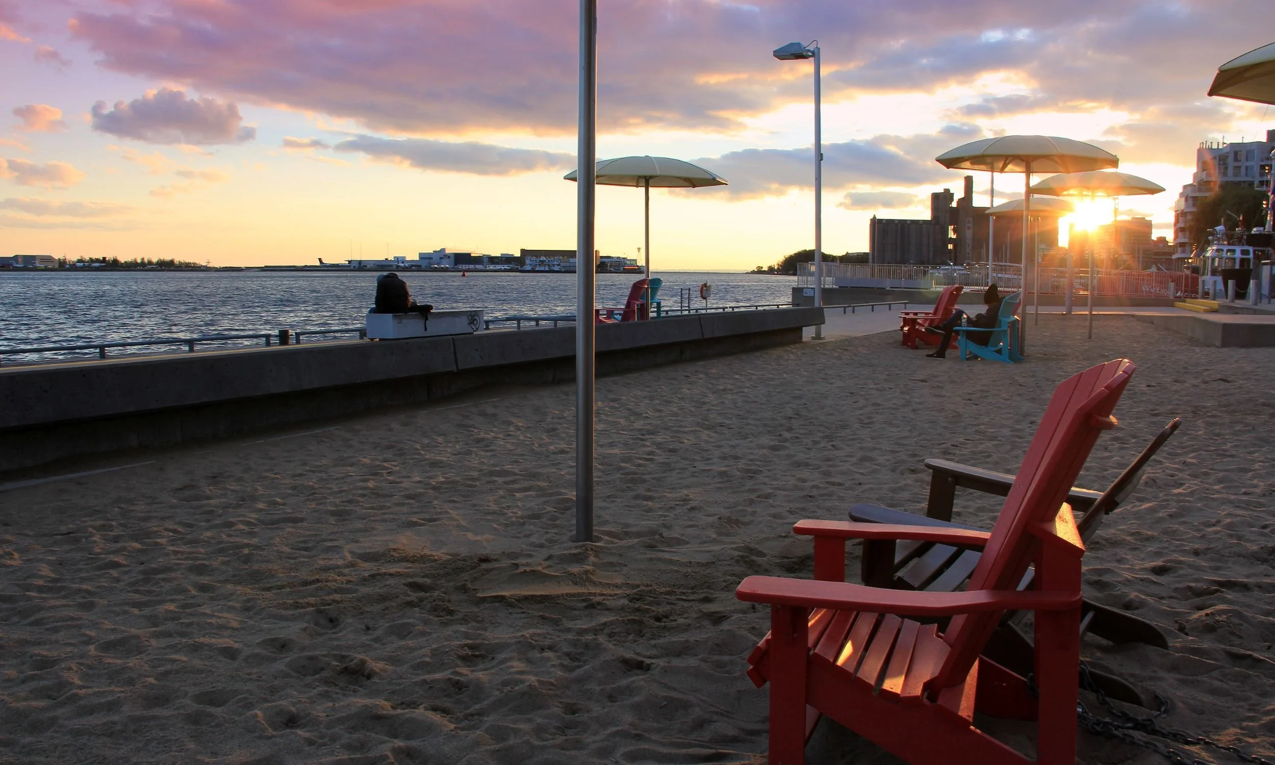 A beach at sunset with umbrellas and two Muskoka chairs.