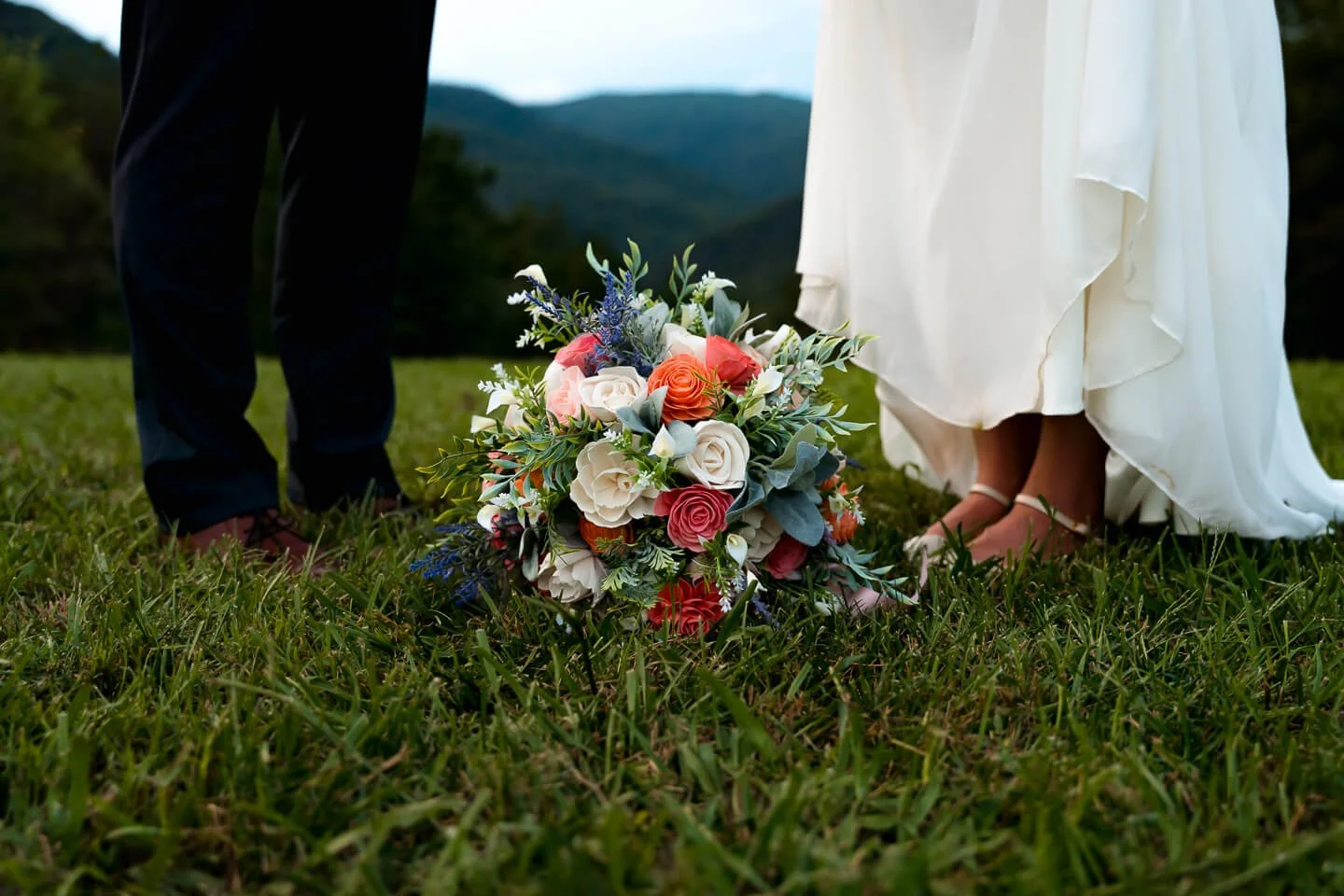 Close-up of a wedding bouquet on grass with a bride and groom standing nearby