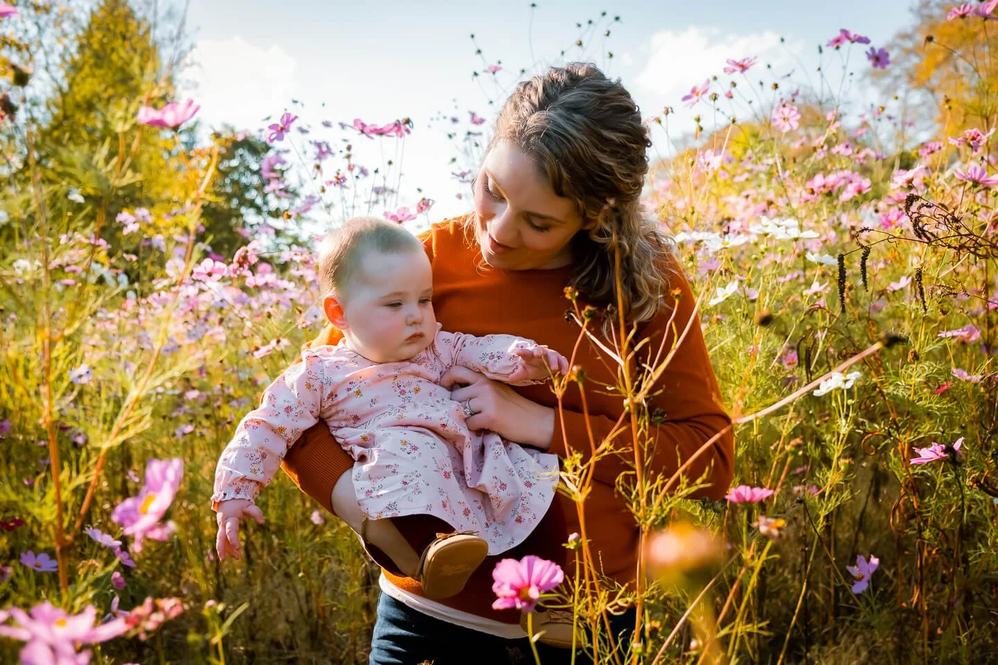 A woman holding a young child in a field of pink and purple flowers during the daytime.