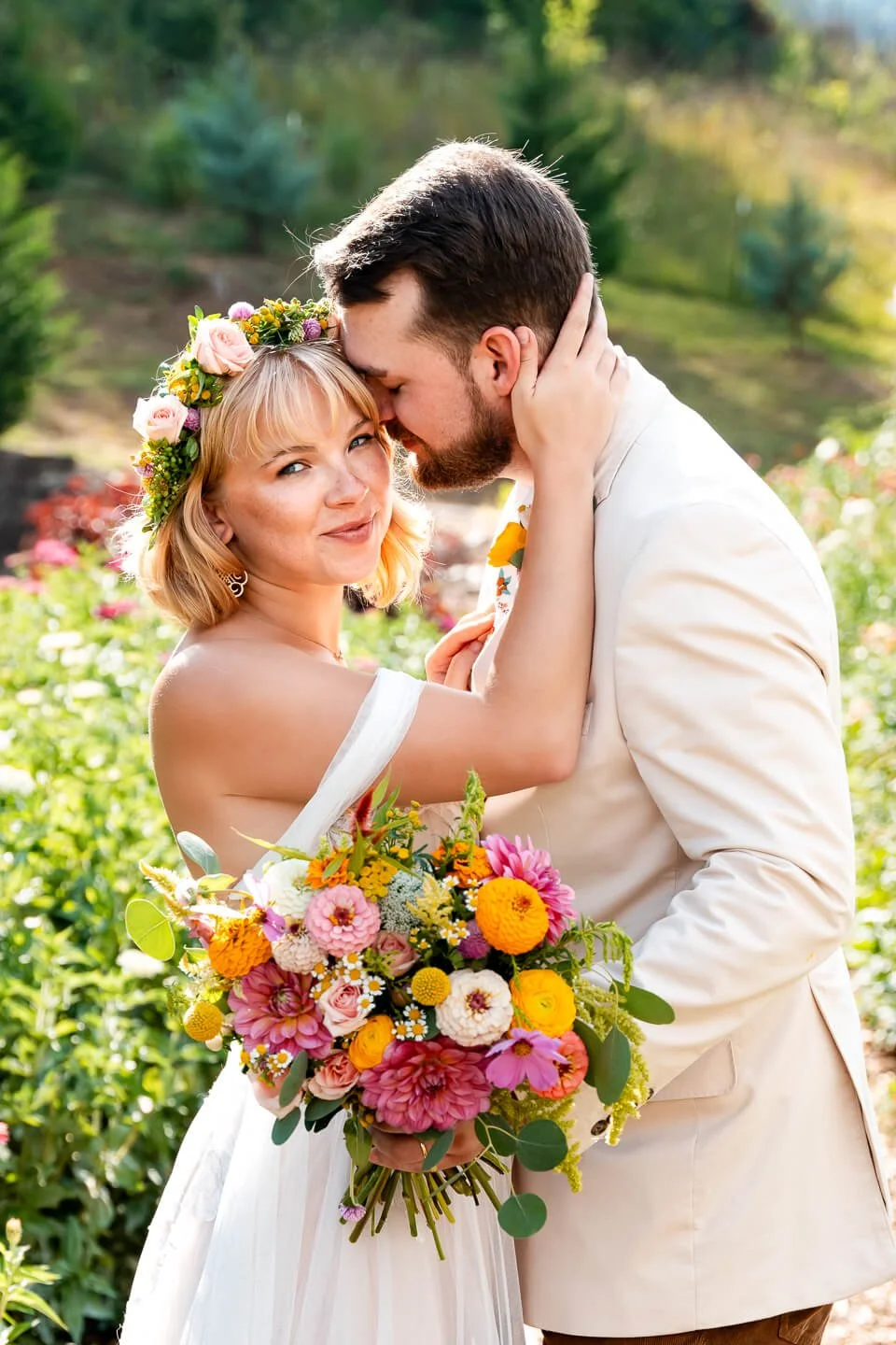 A newlywed couple sharing a romantic moment outdoors, with the bride holding a colorful bouquet and wearing a floral crown.