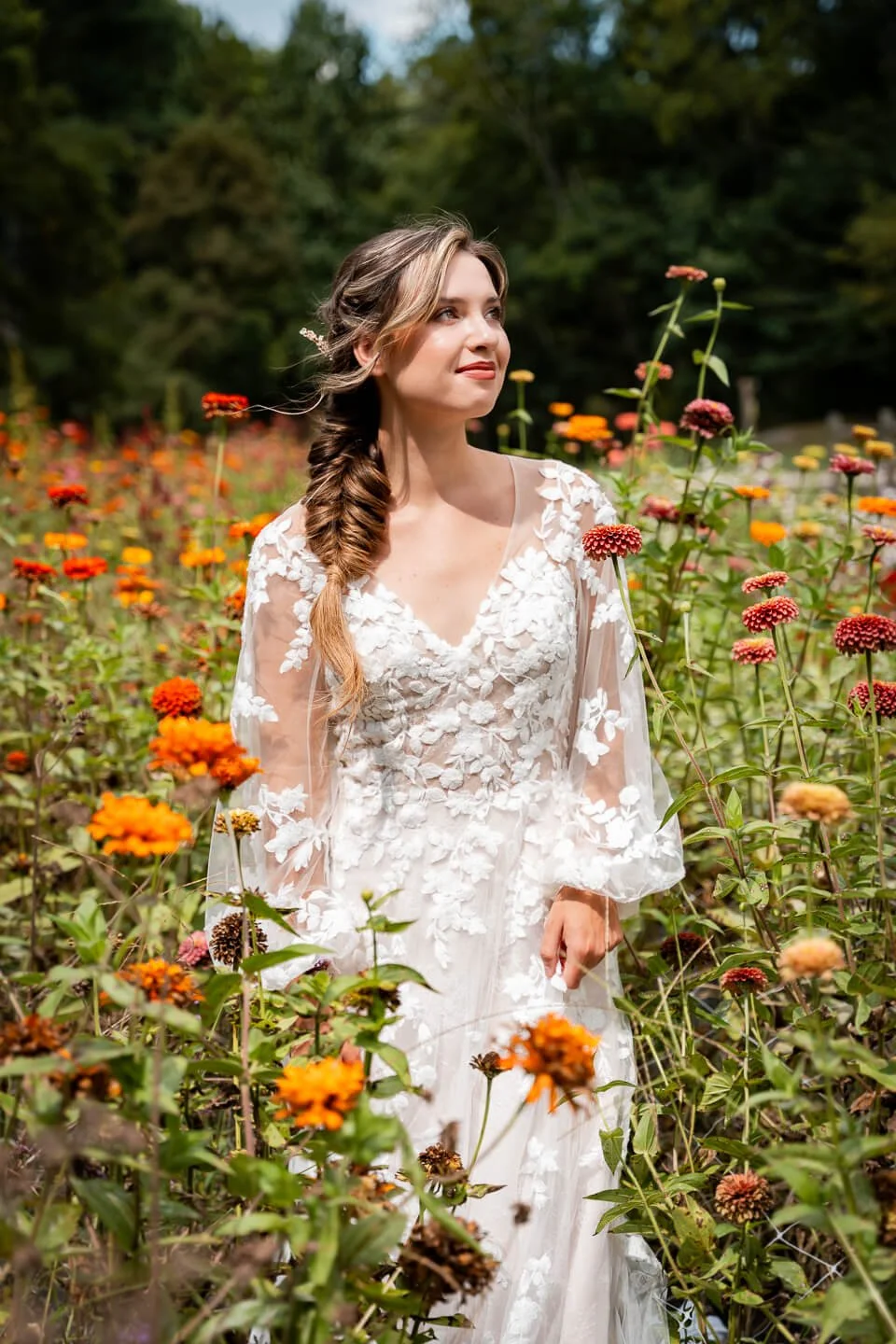 Woman in a white floral dress standing among orange and pink flowers in a garden during daytime.