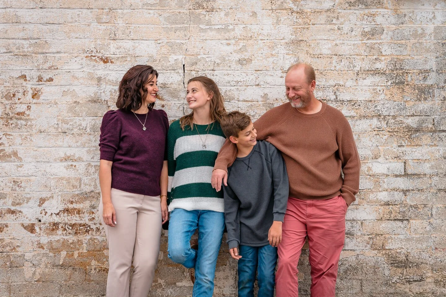 Four people, two women, two boys, standing against a brick wall, smiling and talking to each other.