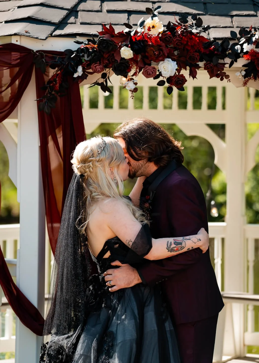 A bride and groom sharing a kiss during their wedding ceremony under a floral arch