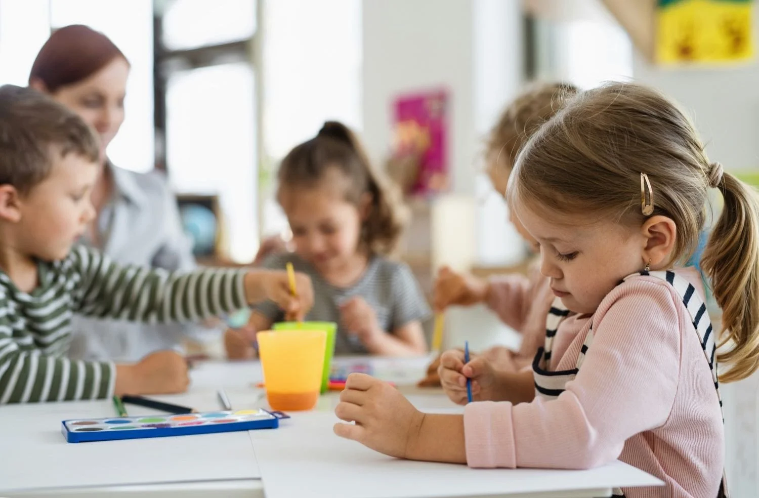 Kids coloring in classroom with teacher.