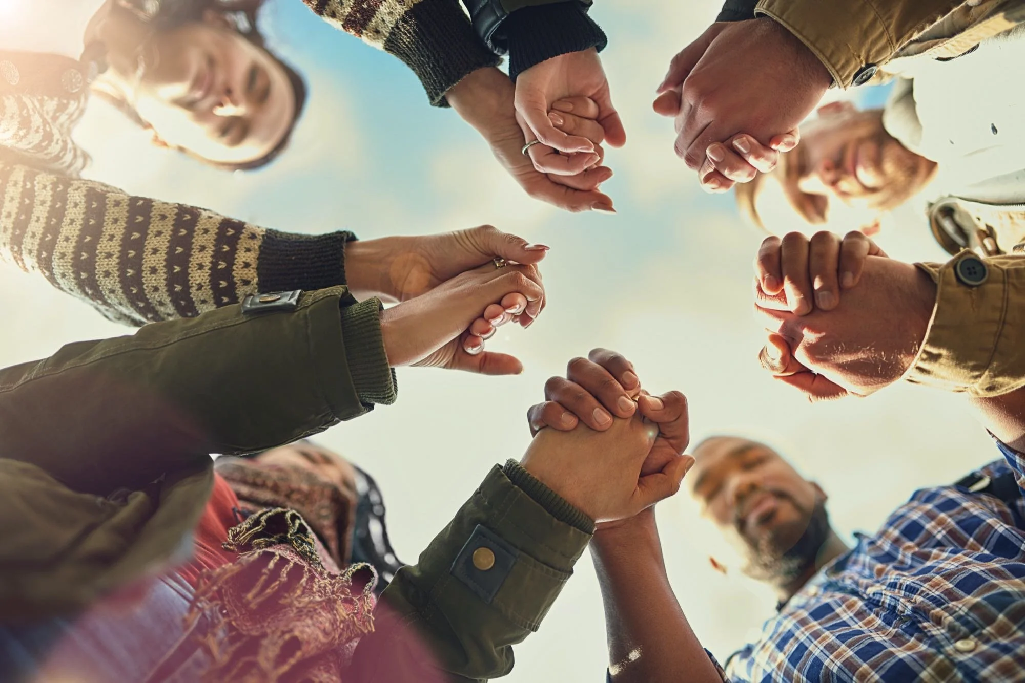 Circle of people holding hands, viewed from below.
