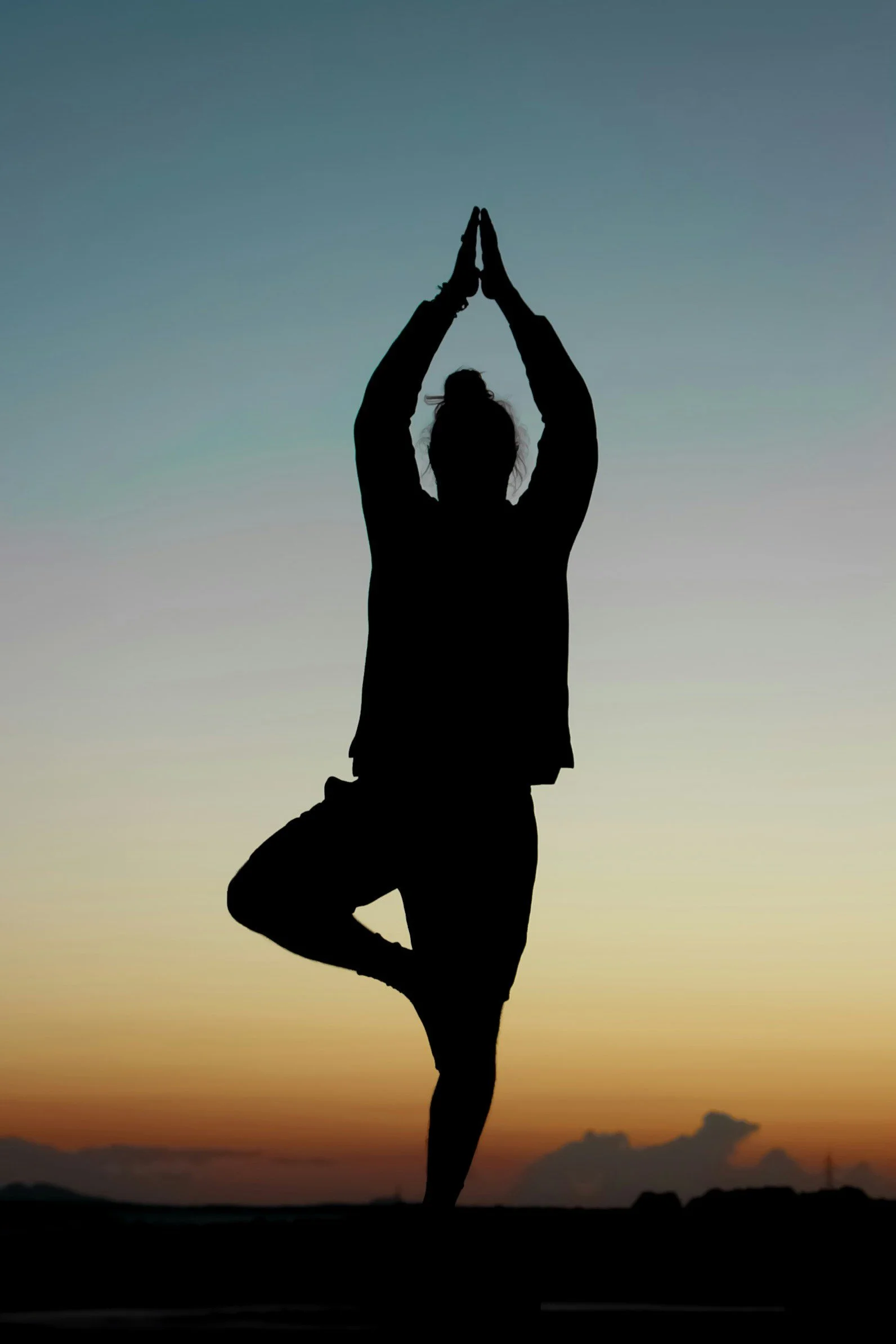 Silhouette of a person practicing yoga in tree pose during sunset.