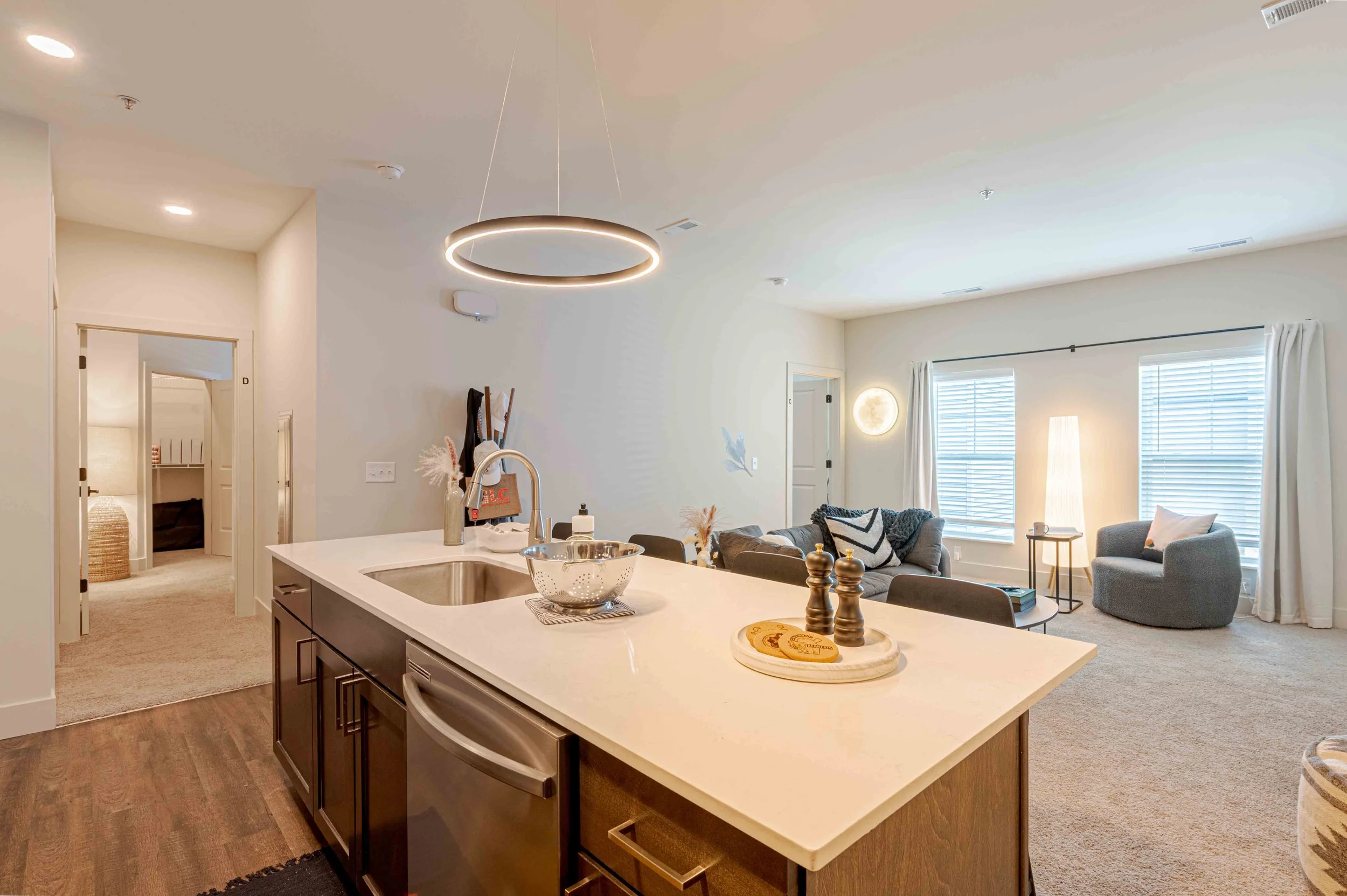 Open-concept living room and kitchen with island, modern lighting, and large windows with white curtains.
