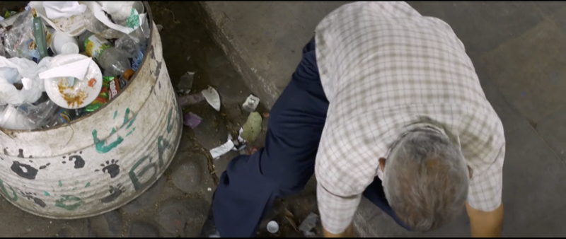Man bending near an overflowing trash can.
