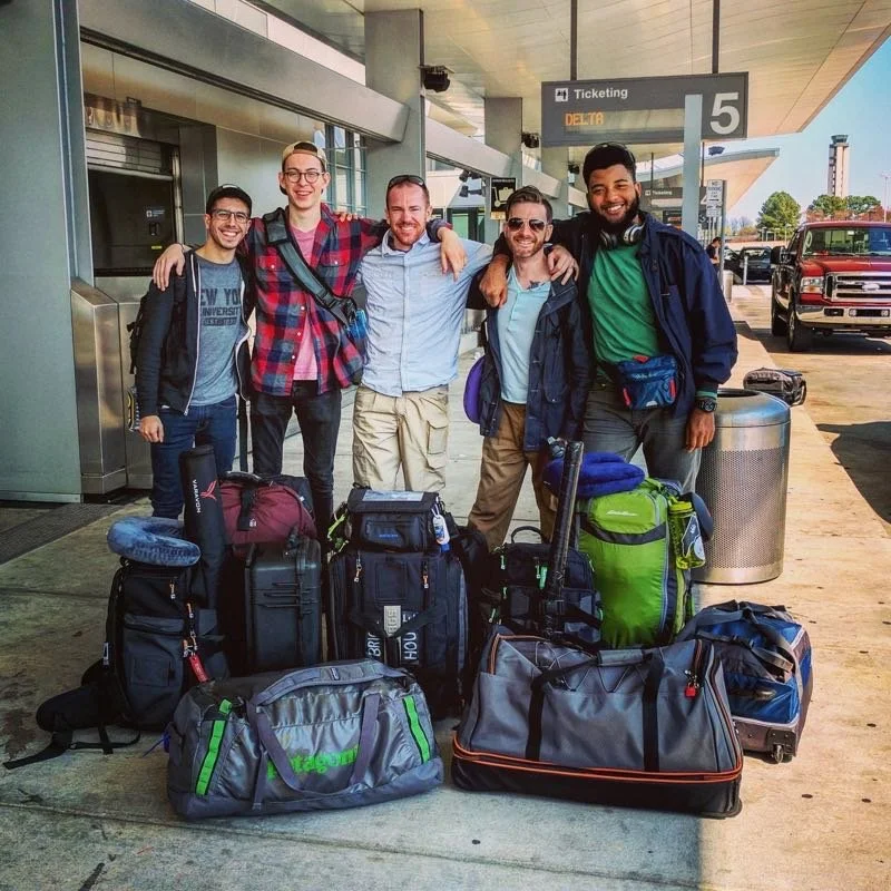 Group of five men with luggage at airport.