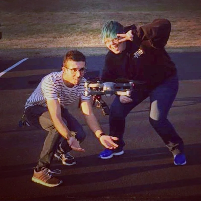Two people posing with a drone outdoors.