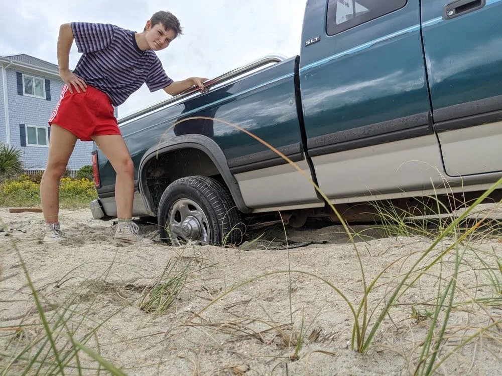 Person next to a truck stuck in sand