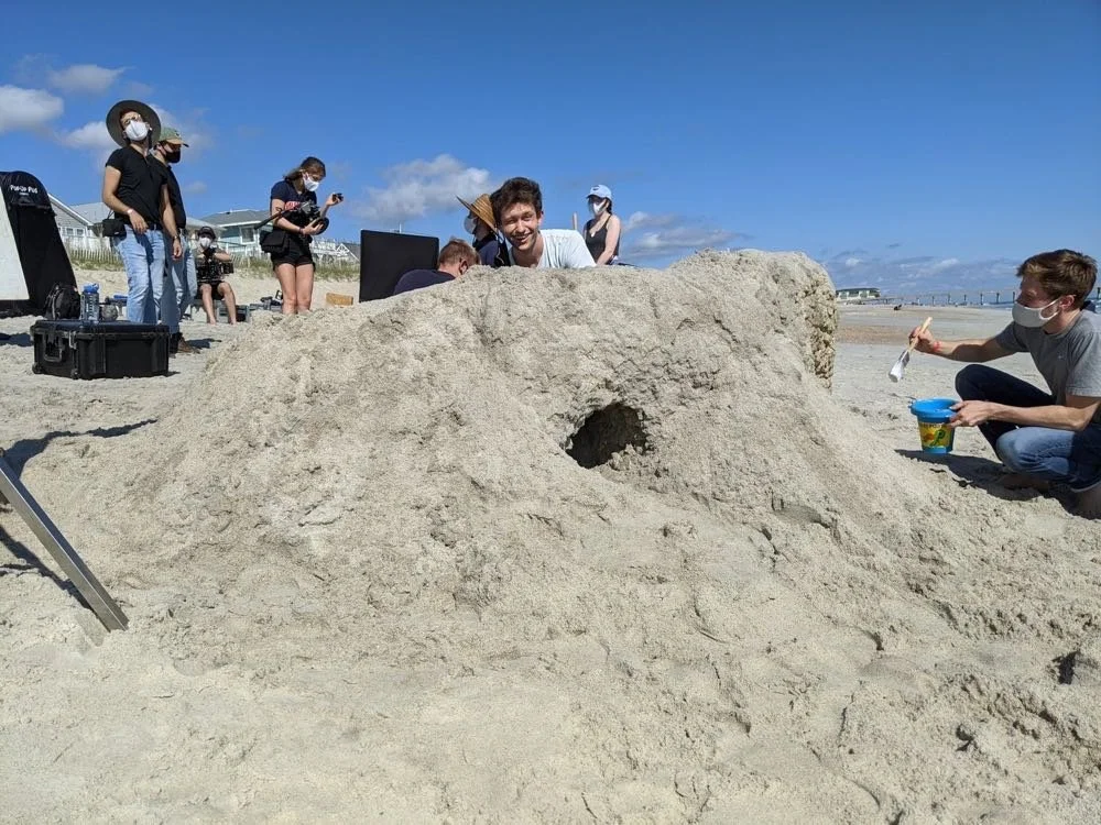 People building a large sand structure on a beach.