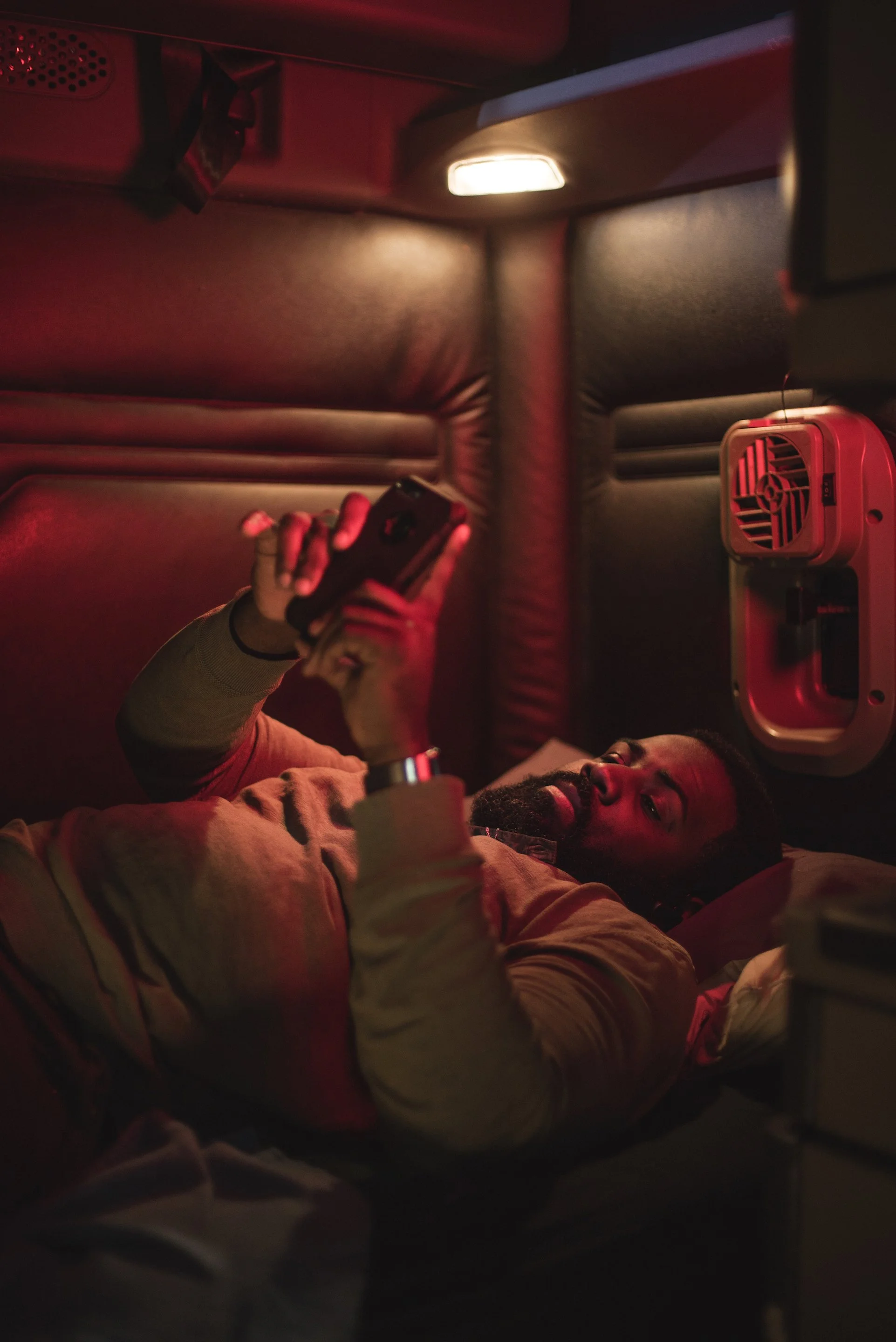 Man using a smartphone in a red-lit cabin.