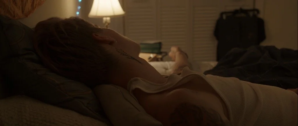 Person resting head on another's back in bed.