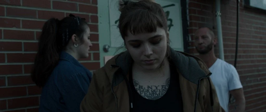 Three people outdoors, one appearing contemplative.