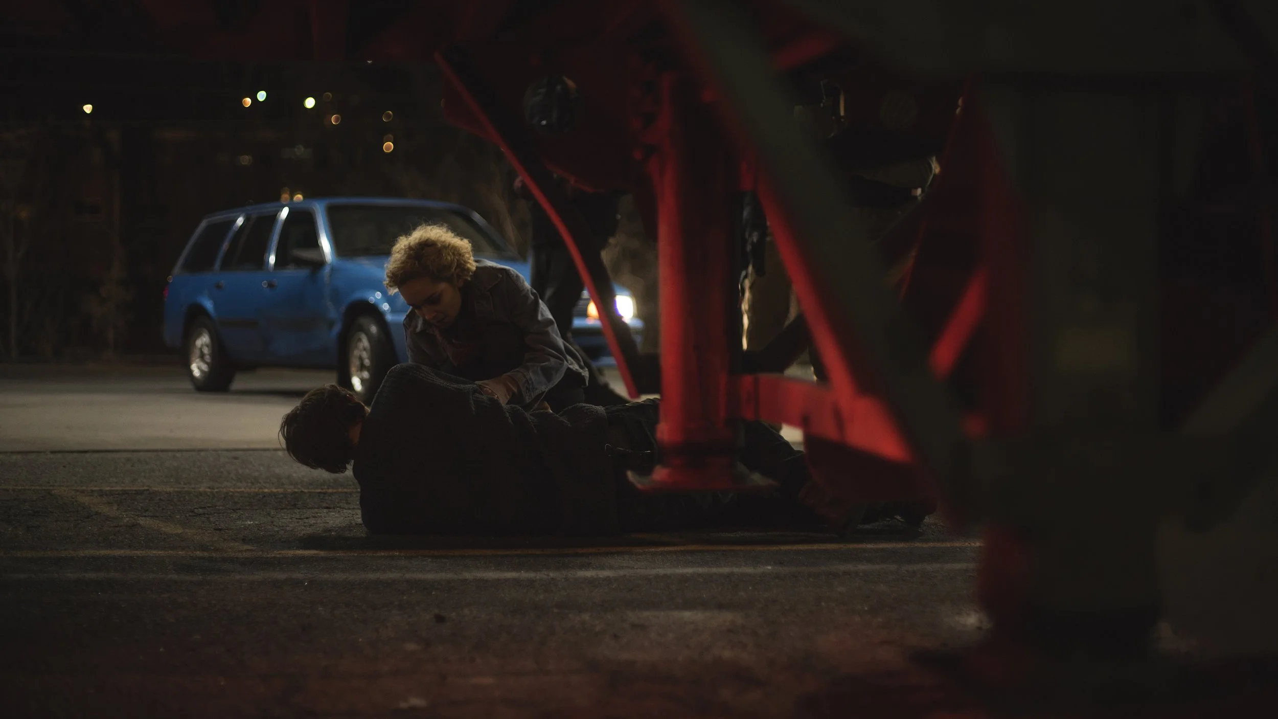 "Person aiding another under a truck at night"