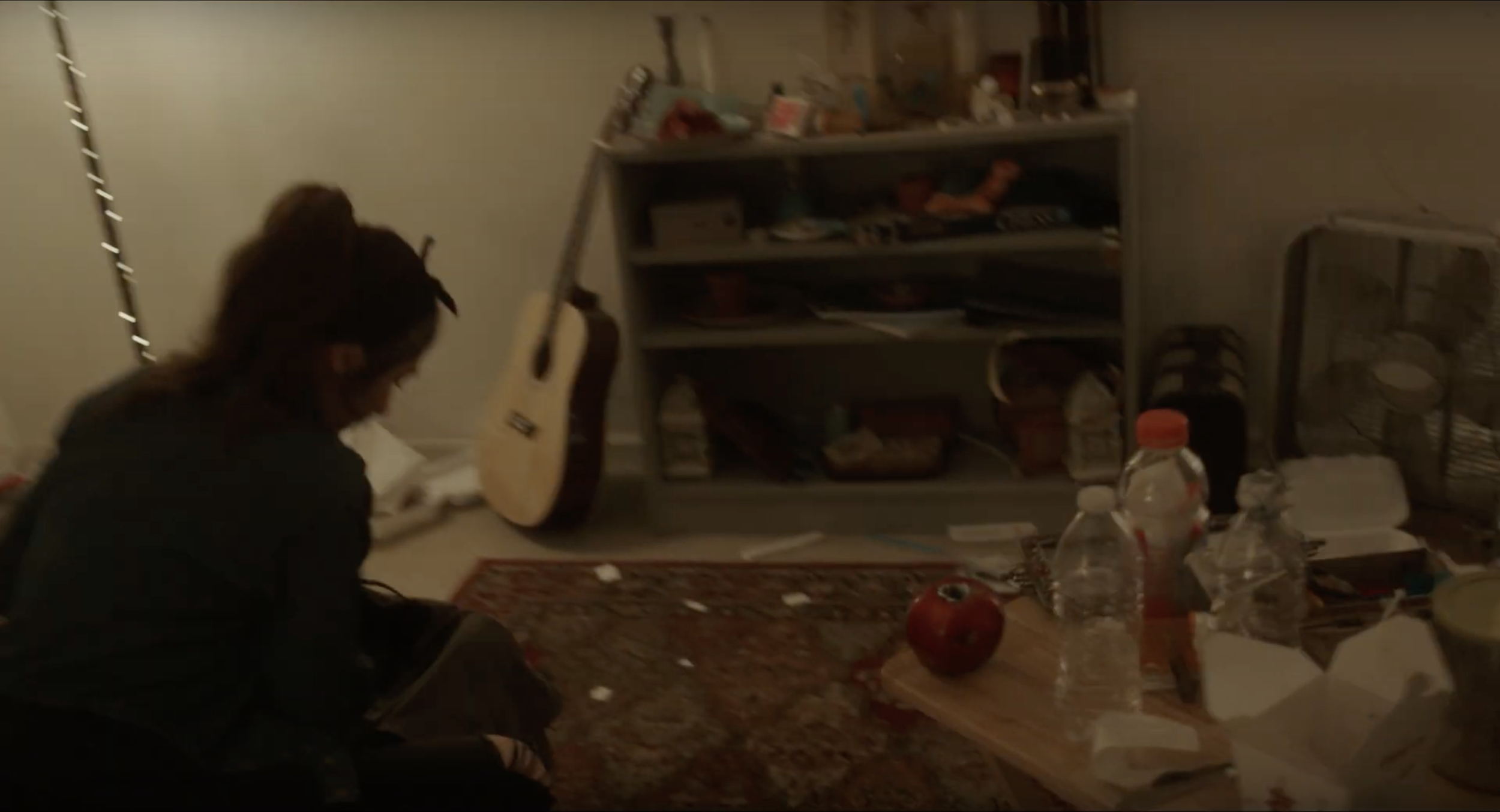 Woman sitting by messy shelf and guitar