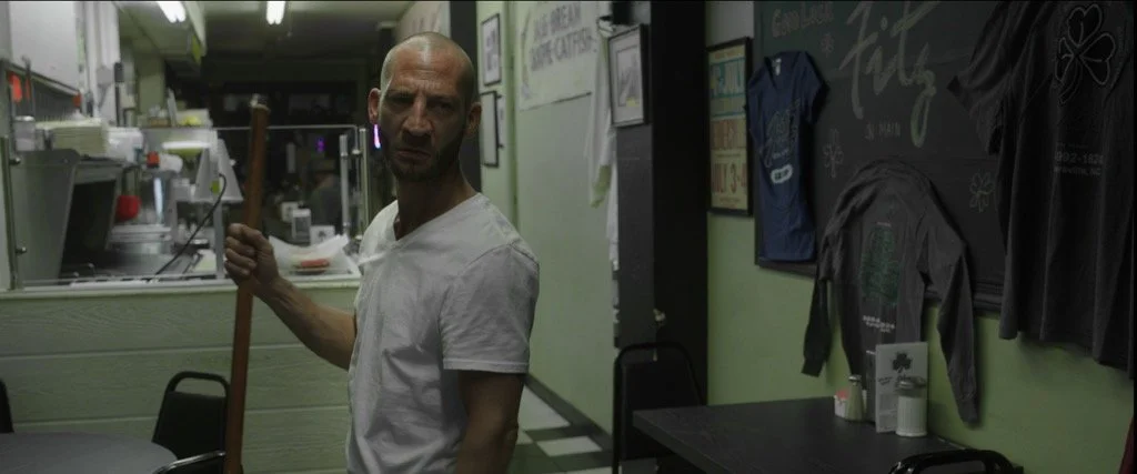 Man standing in a diner with a mop handle.