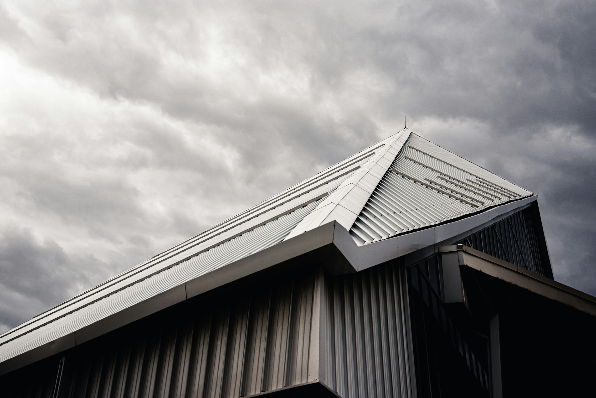 Close-up view of a modern building's sloped metal roof with a cloudy sky in the background.