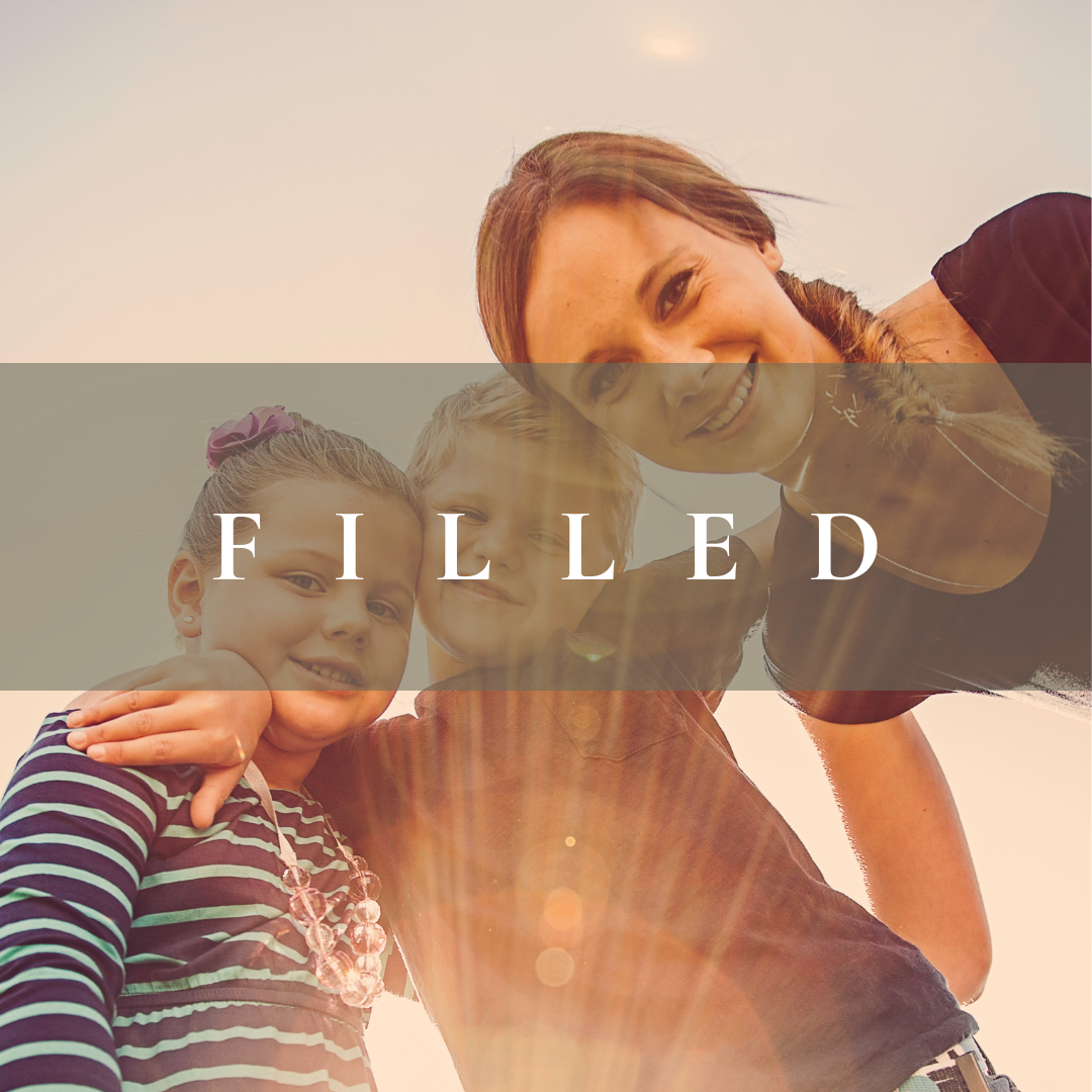 A woman and two children smiling and taking a selfie outdoors with the sun shining.