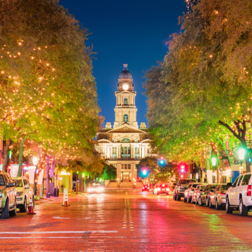Historic downtown Fort Worth street at night featuring Sundance Square Plaza and beautifully lit trees lining the brick roadway.