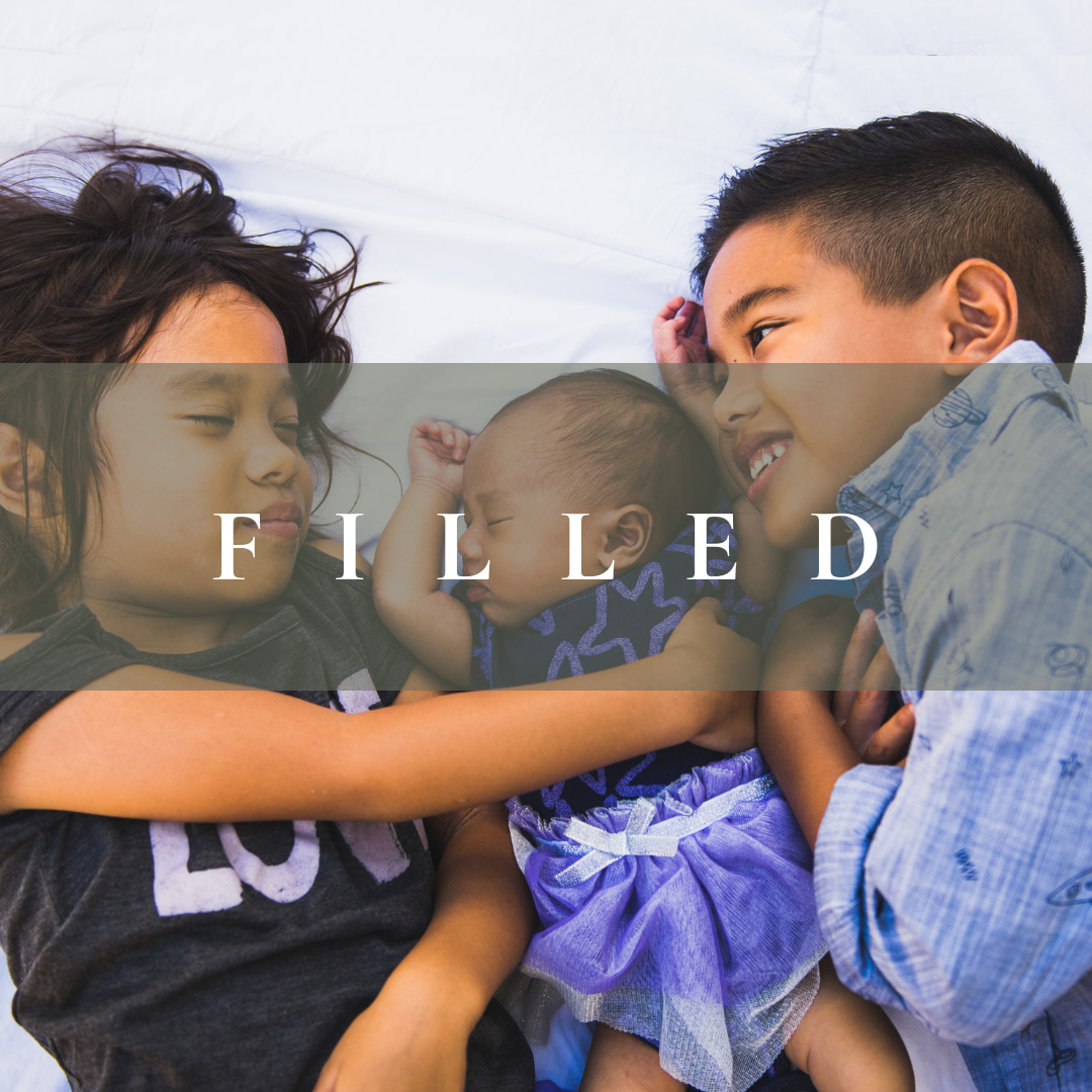 Three children, a girl, a baby, and a boy, lying on a bed and cuddling.