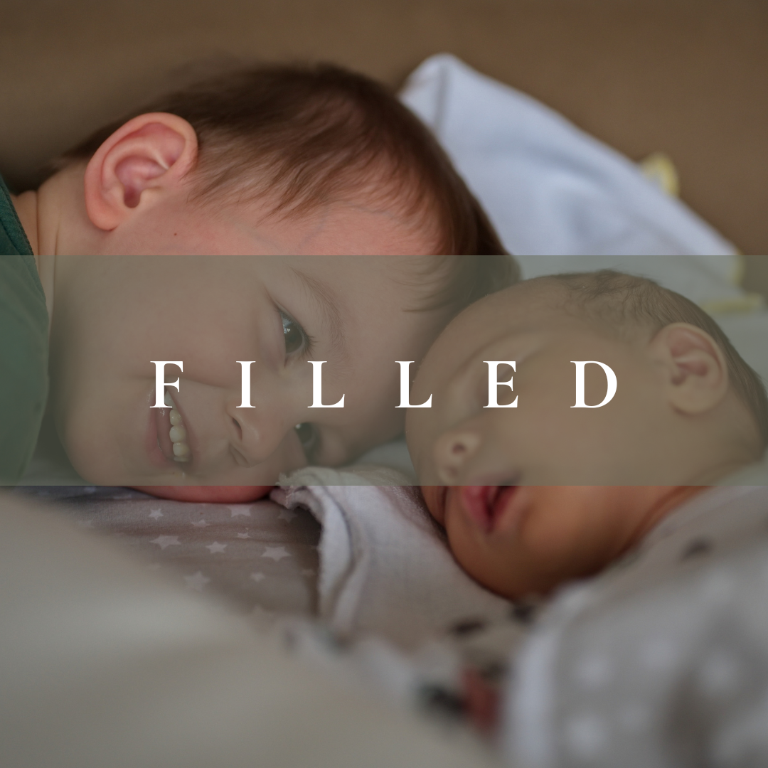 A young boy smiling and lying close to a sleeping baby, both lying on a bed.