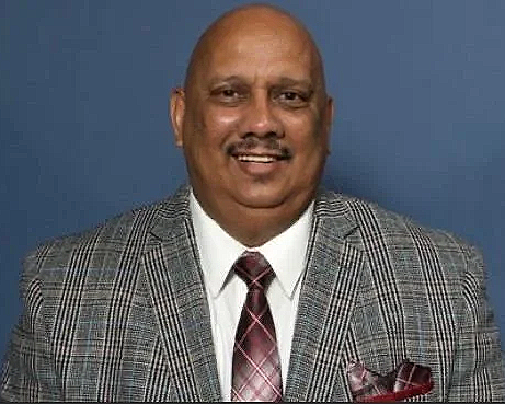 Smiling man in a grey patterned suit with a burgundy tie and matching pocket square