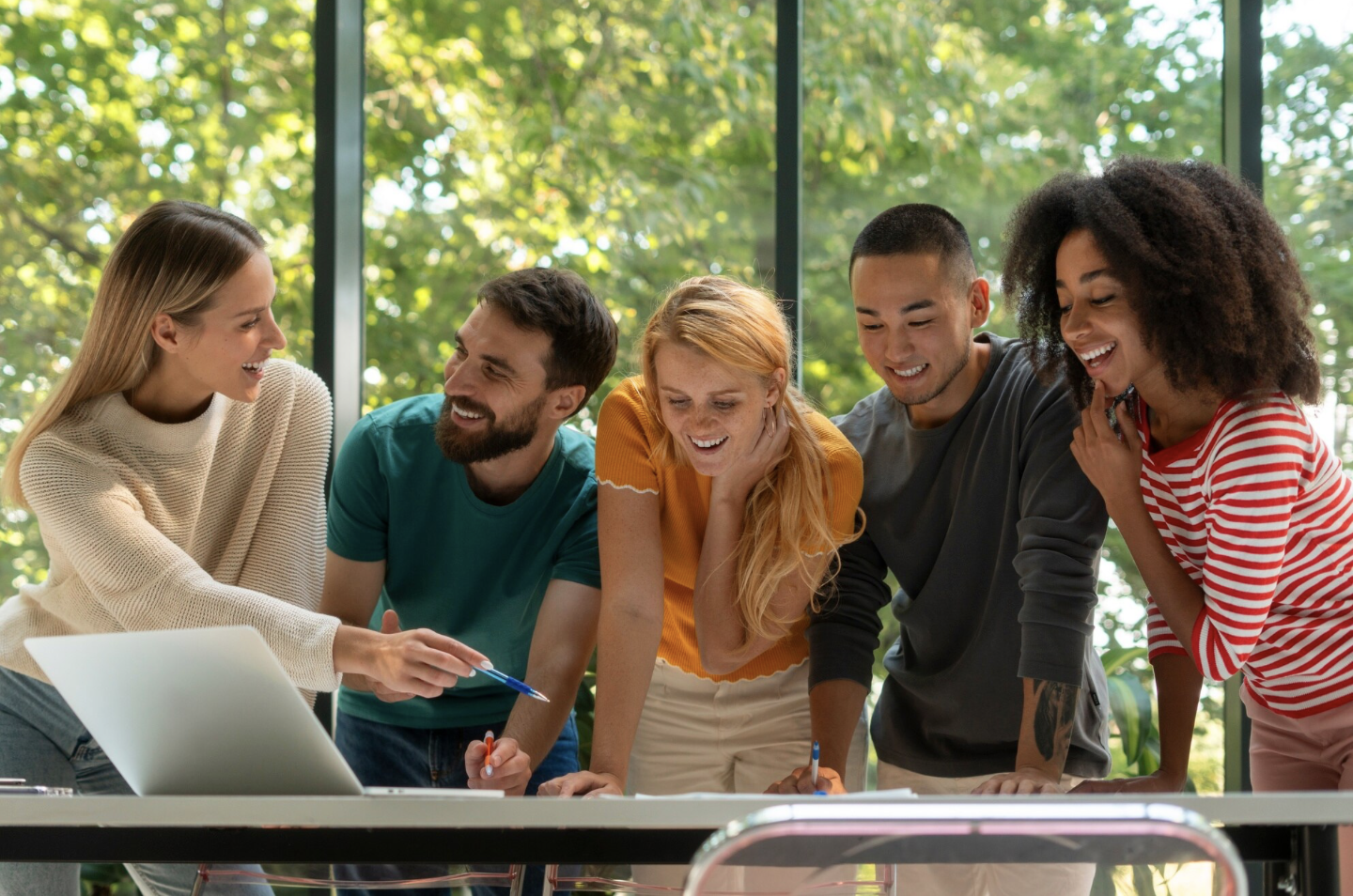Groupe de cinq personnes souriantes en réunion ou en discussion dans une pièce avec grandes fenêtres et vue sur la verdure.
