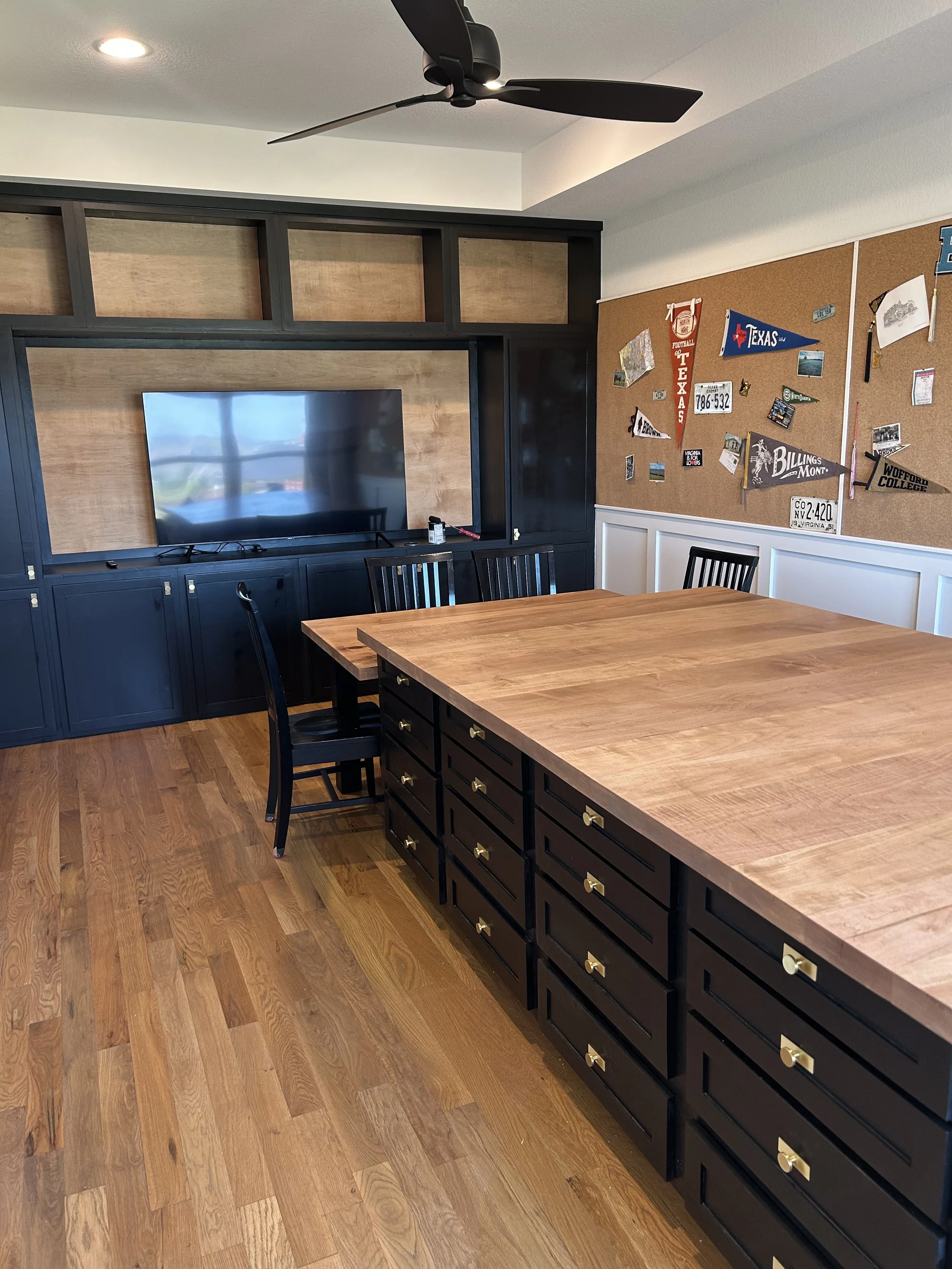 craft room island and entertainment center. black cabinets and gold pulls with a craft table and built in shelving. gold hardware and black island cabinets