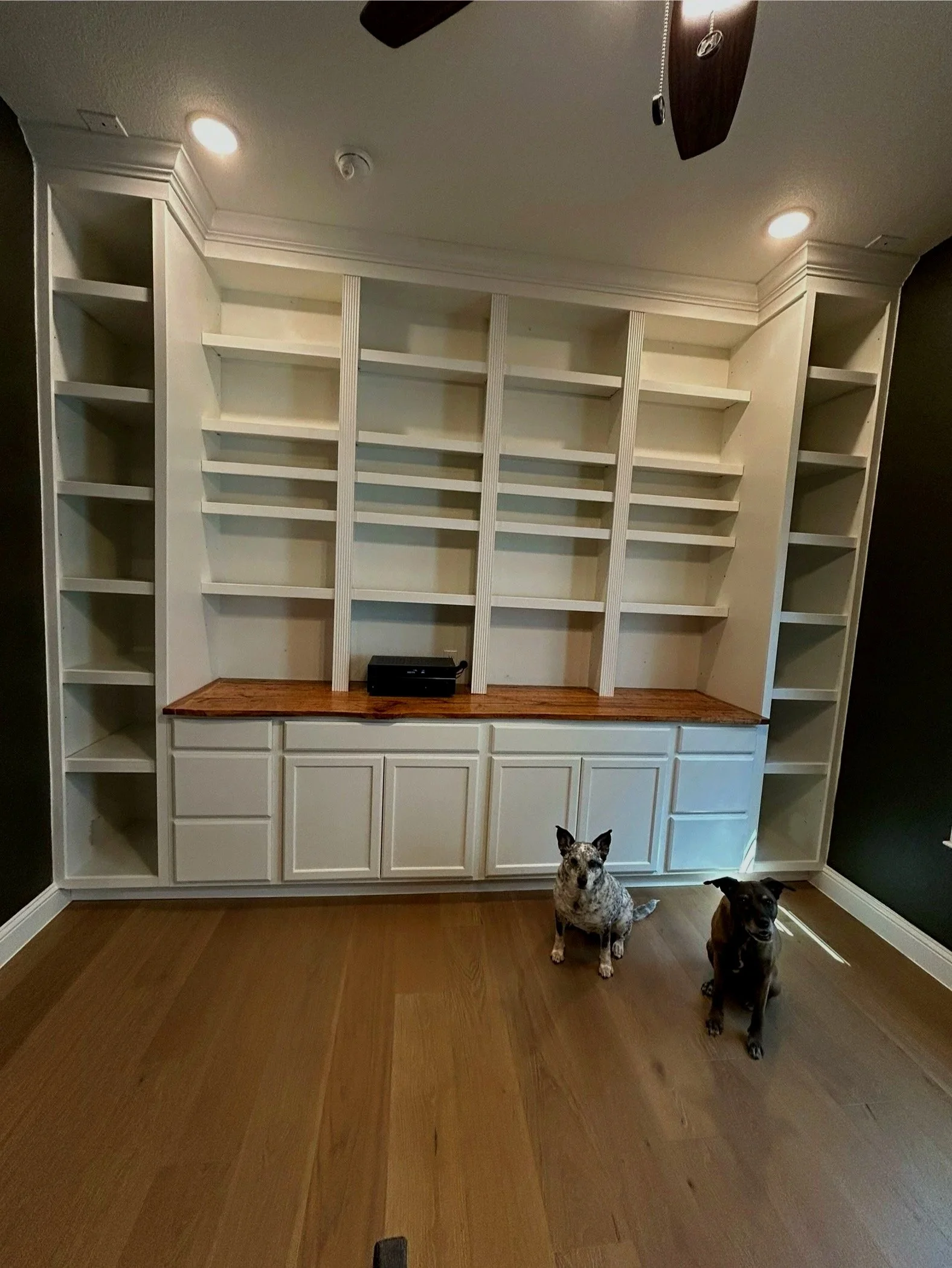 A built-in white bookcase with open shelving and a wooden countertop. Built in for office or playroom.