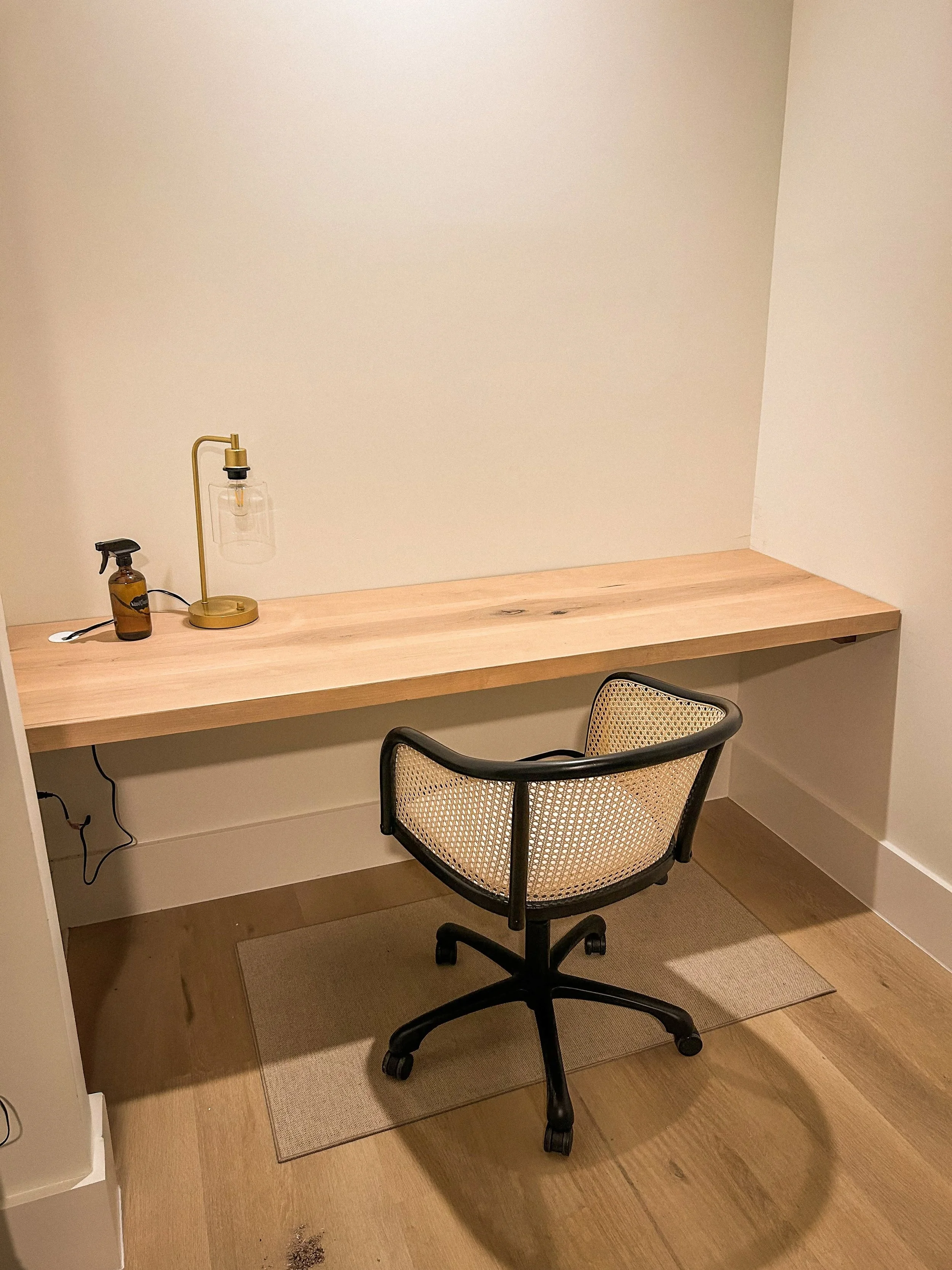 Built in desk for a guest bedroom, light wood and a black and wicker office chair. Perfectly placed grommet hole to control wires