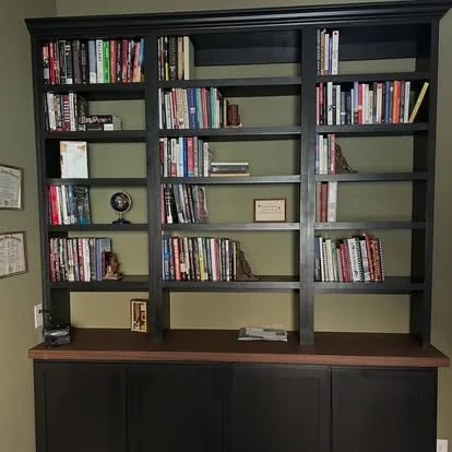 Built in black library built ins, in a home office. Green walls and solid oak countertop on top of the black cabinets. 