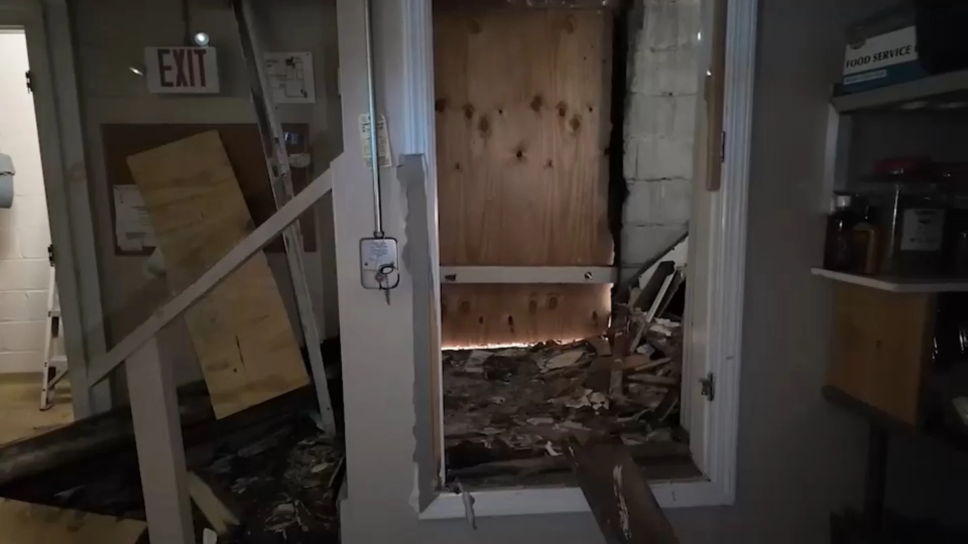 Damaged building interior with boarded windows, rubble, exposed walls, and an illuminated exit sign