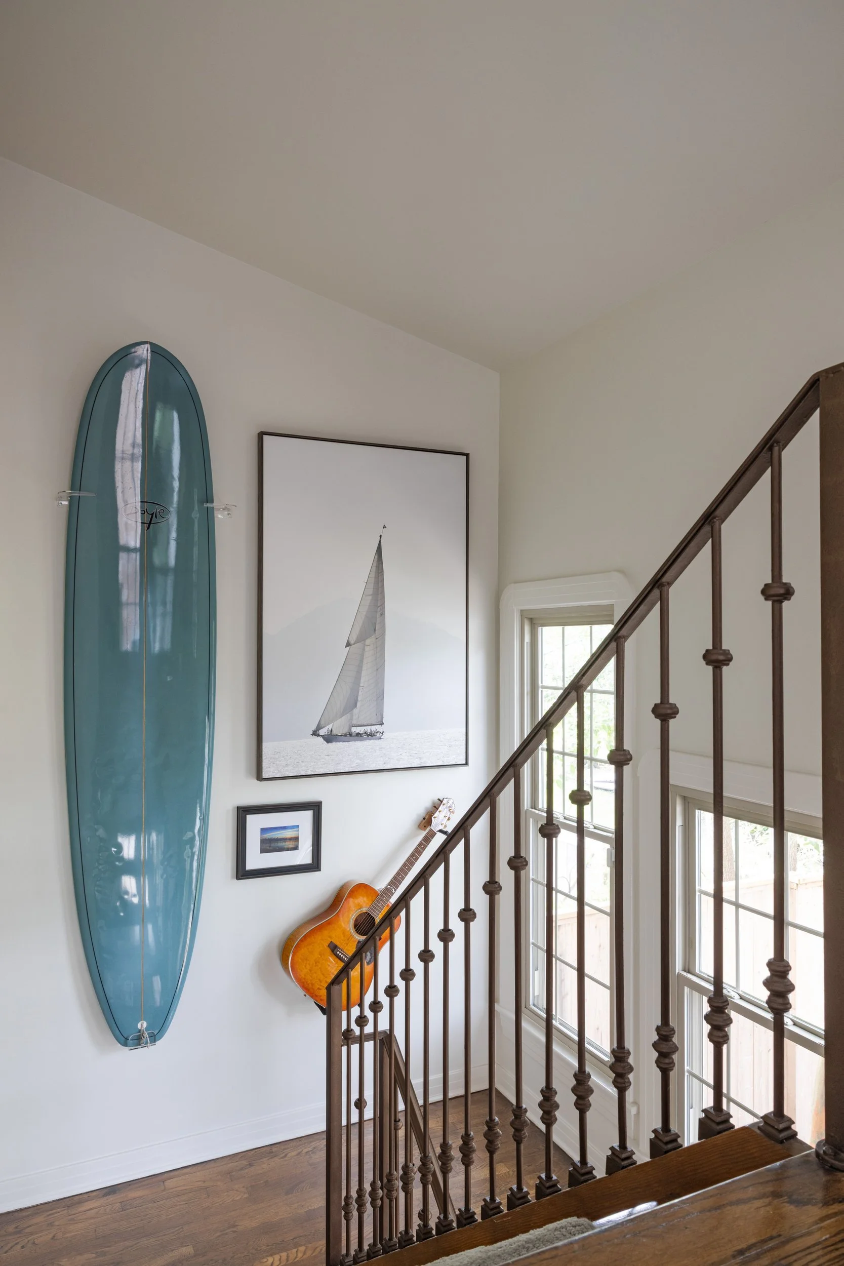 Stairwell with a blue longboard, sailboat photograph, and guitar