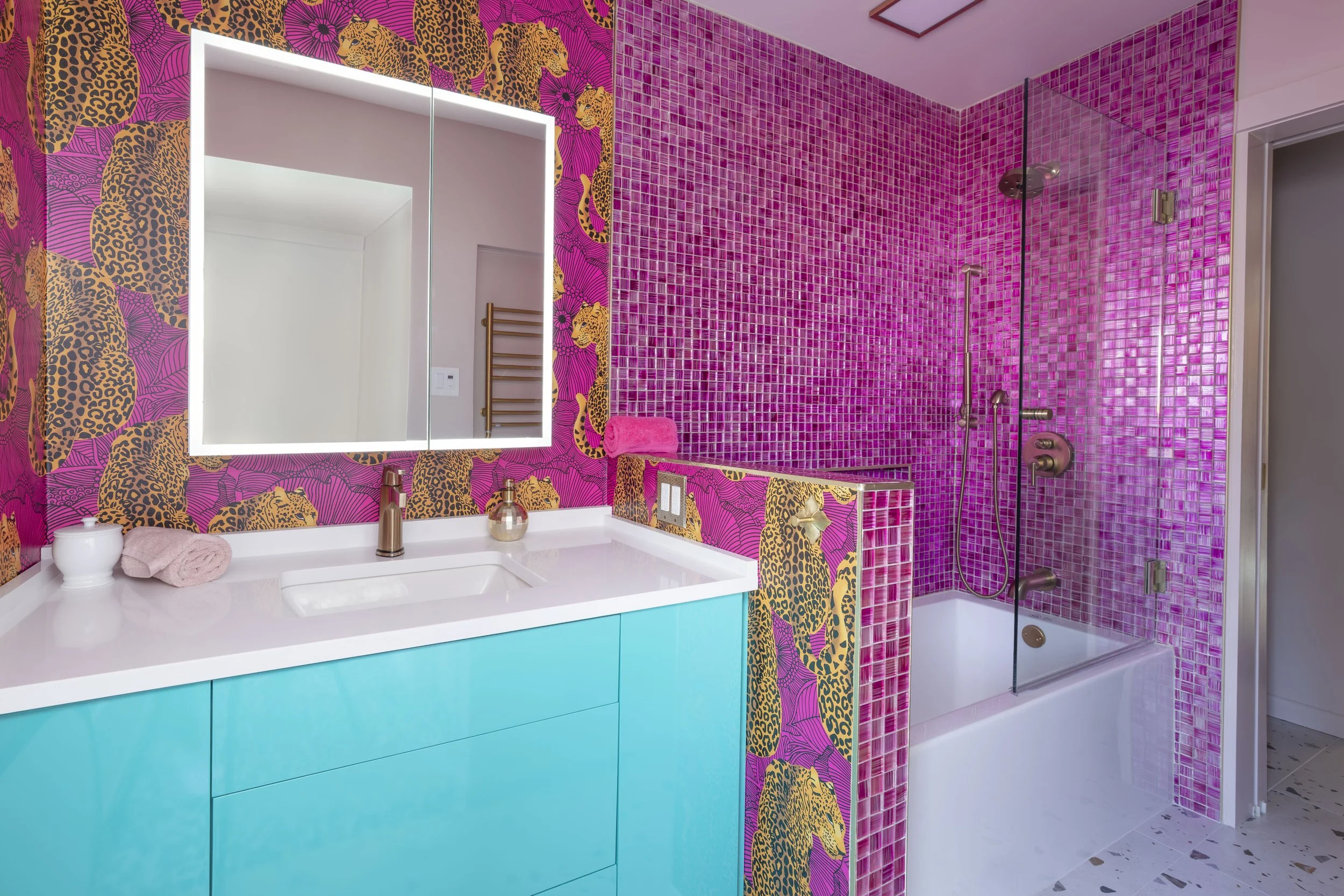 Her side of the primary bath with pink leopard wallpaper, turquoise vanity, and pink glass mosaic tub