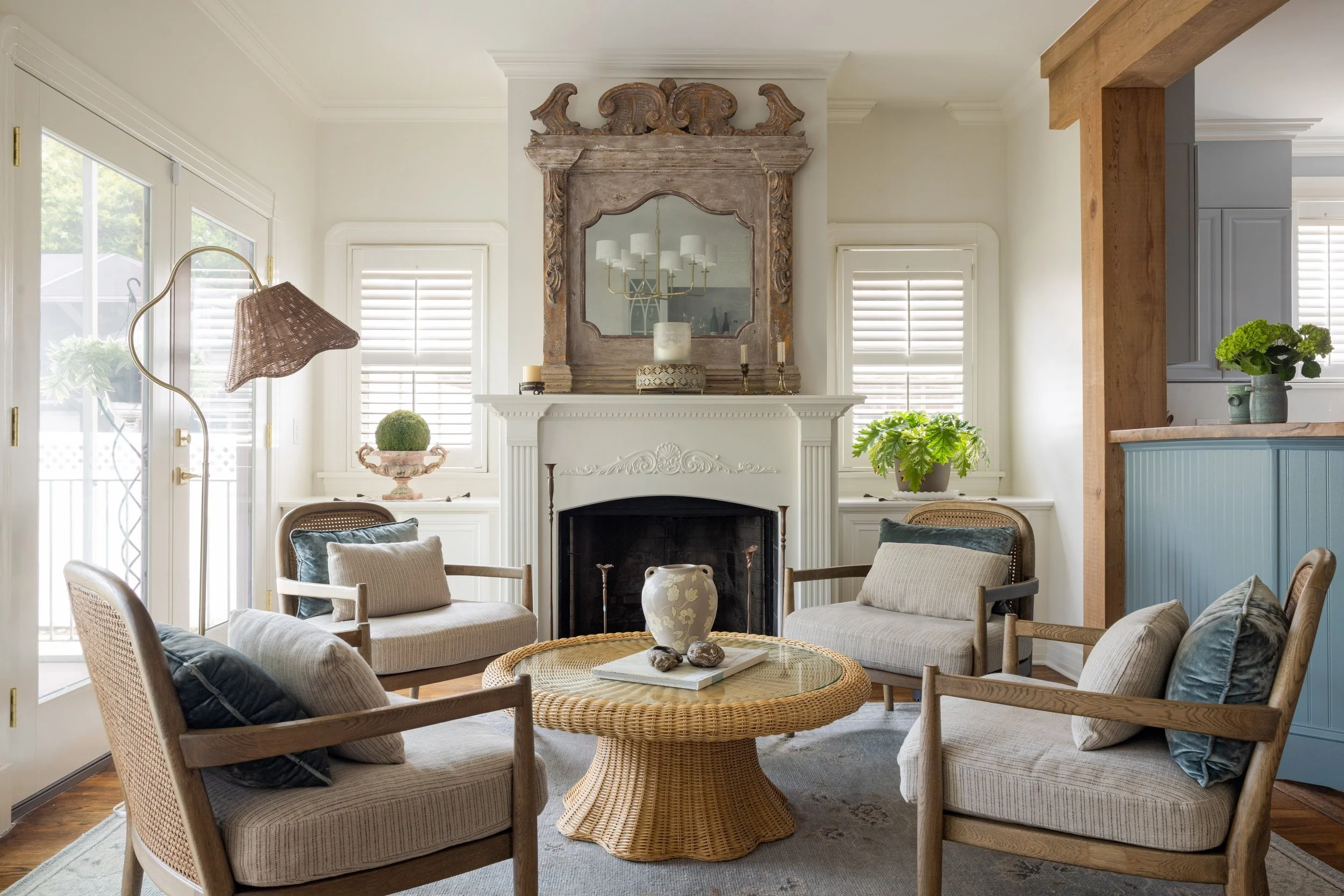 Den with four cane-back chairs around a wicker table, antique mirror over the fireplace
