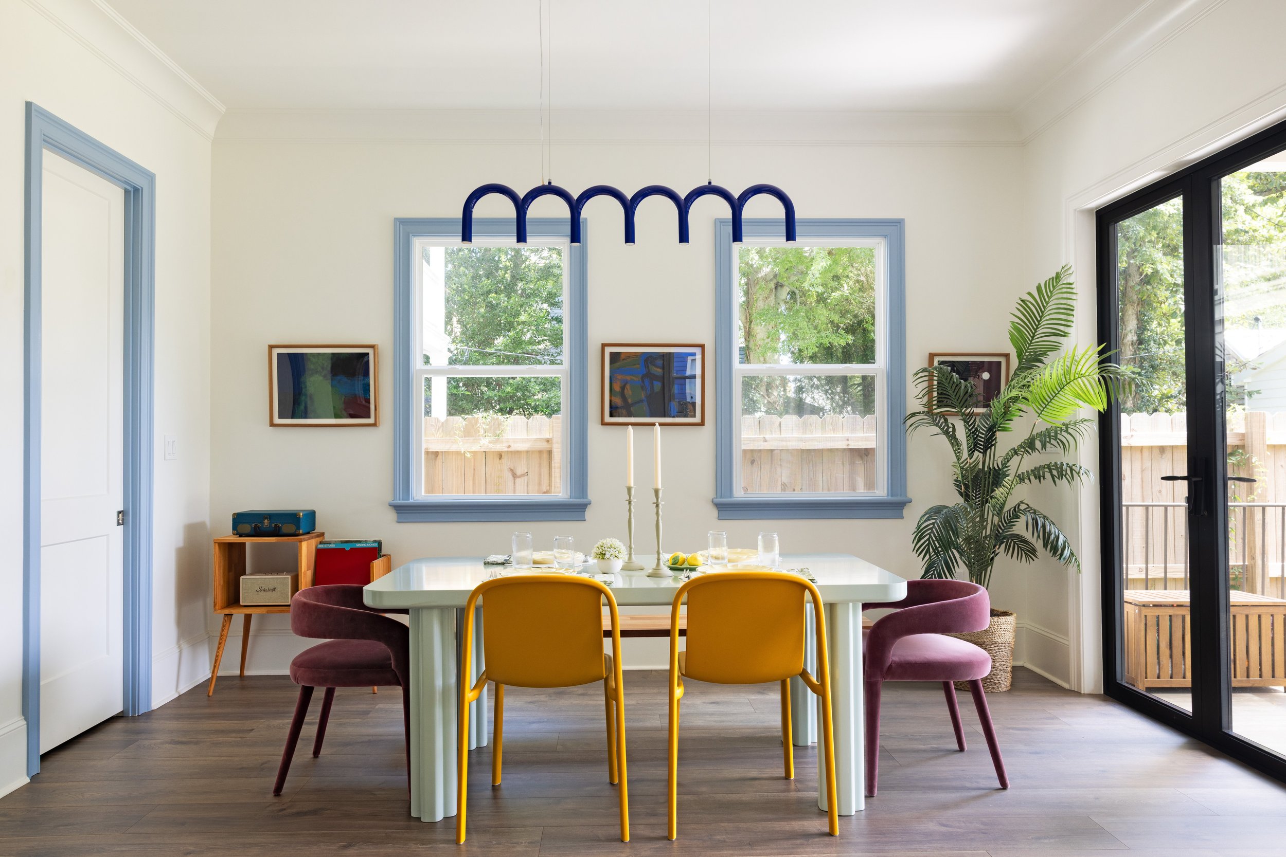 Uptown New Orleans dining room with blue arch pendant, blue window trim, and mismatched chairs