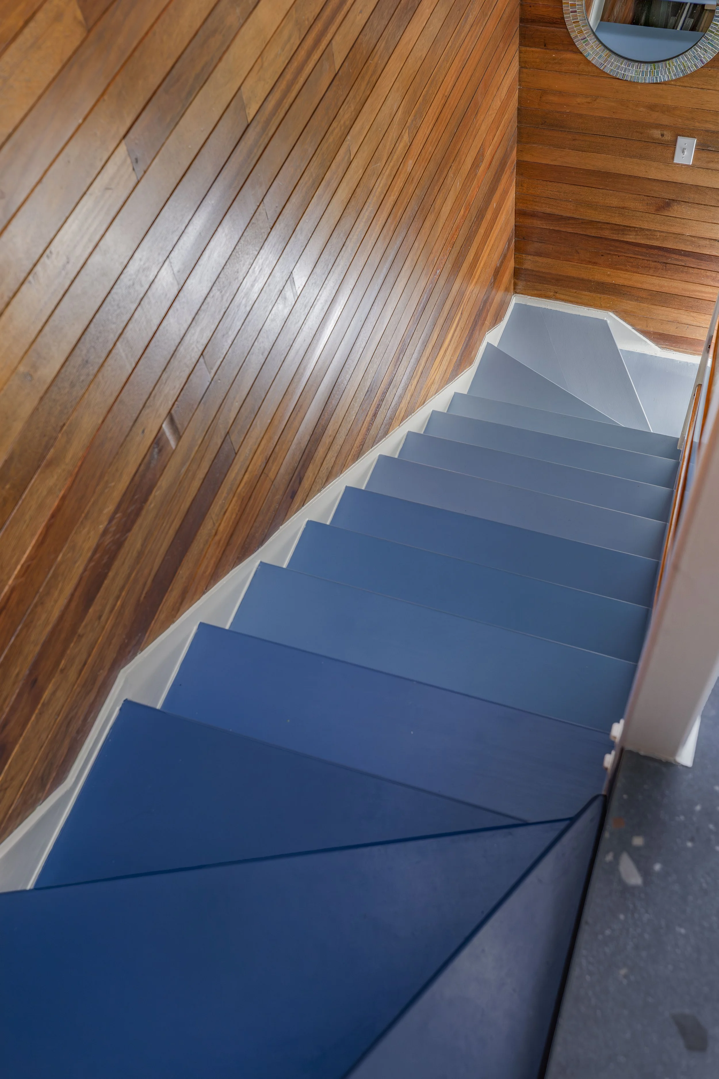 Staircase painted in blue ombré against wood-paneled walls