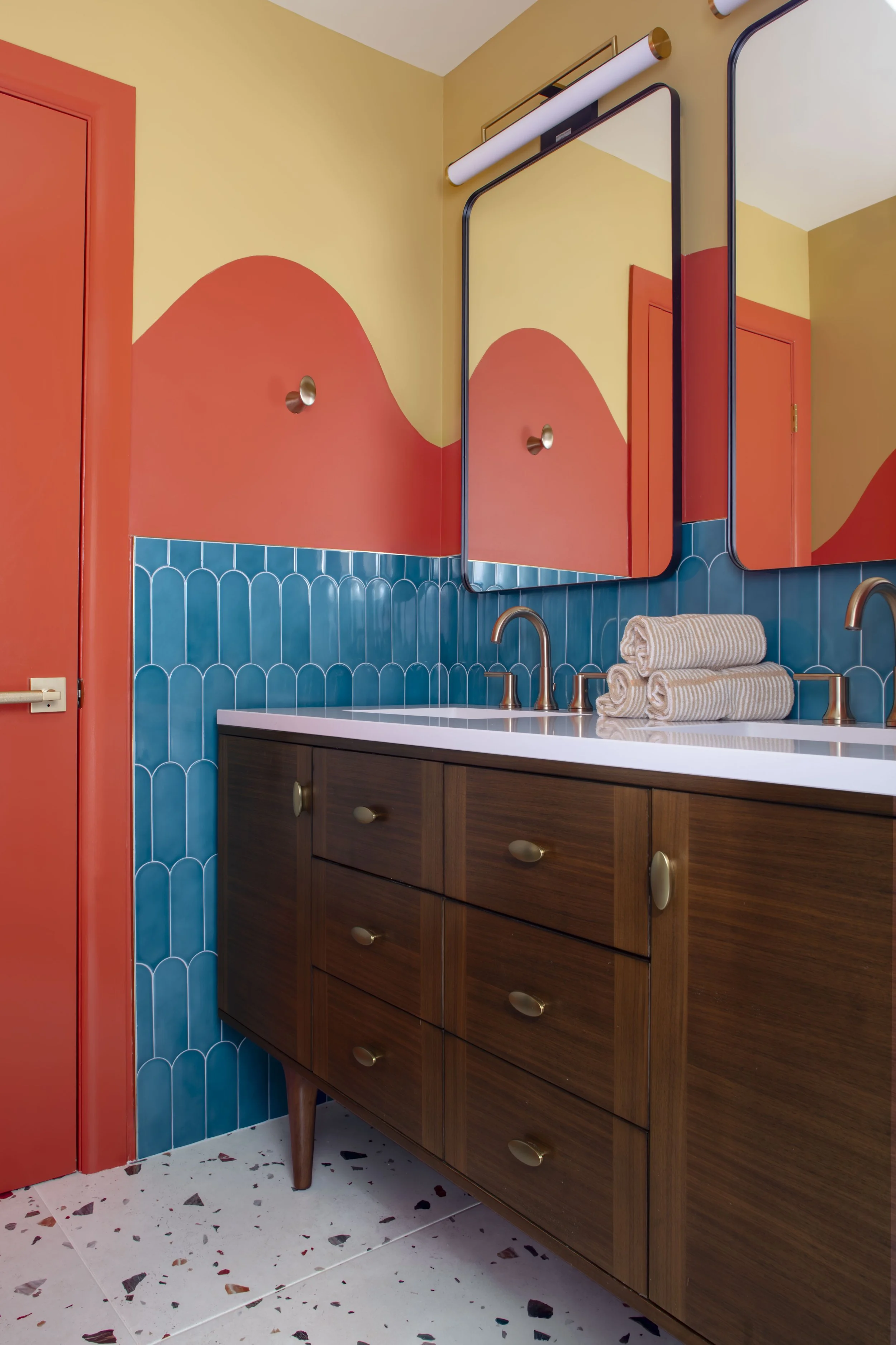 Kids' bathroom with painted mustard and terracotta hills, teal fish-scale tile, and walnut vanity