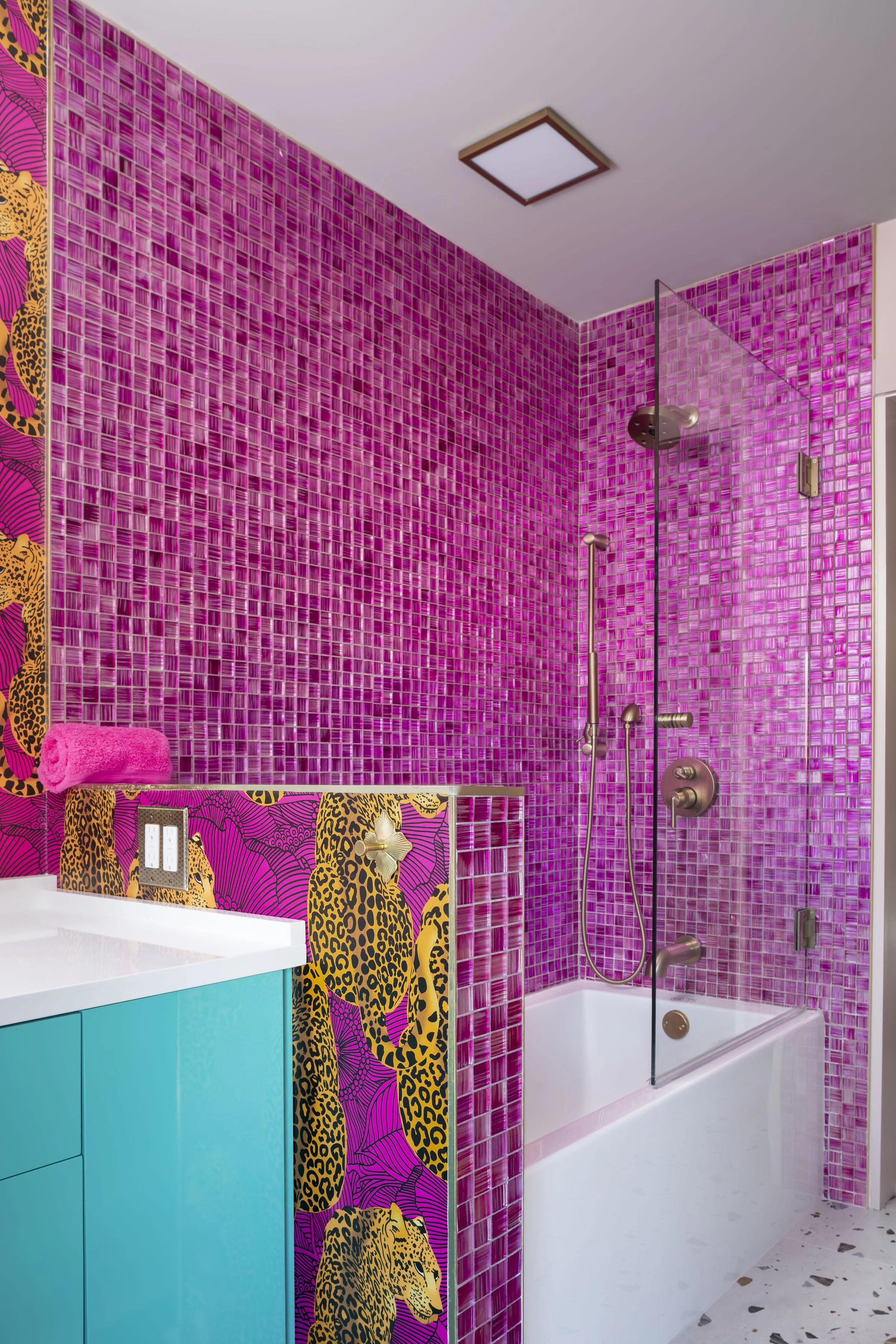 Tub and shower wrapped in pink glass mosaic tile with brass fixtures