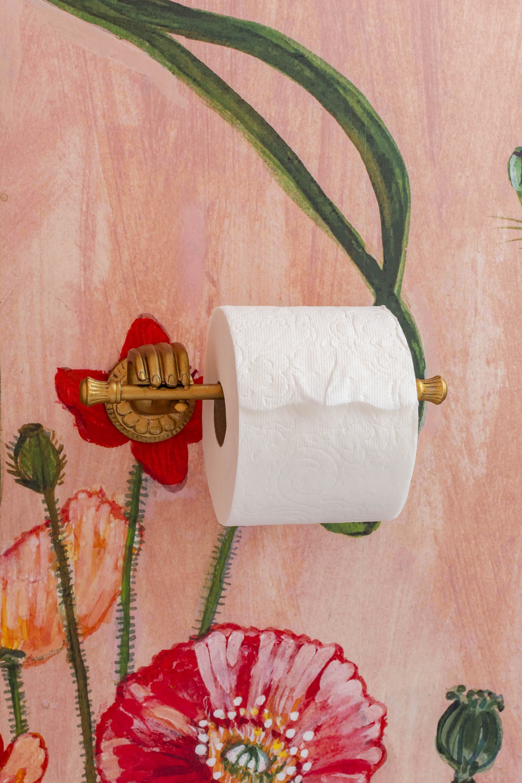 Brass hand toilet paper holder on floral wallpaper