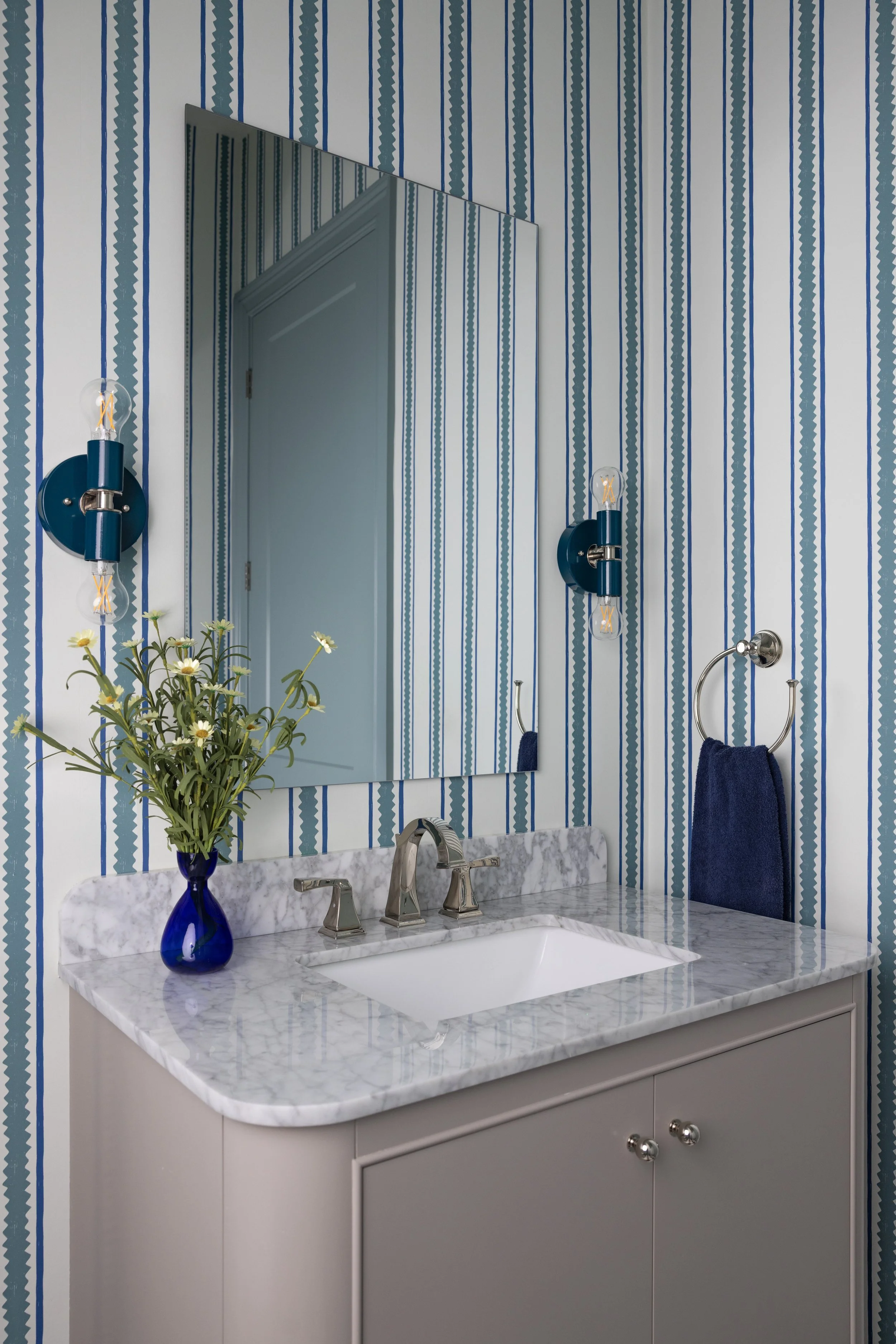 Powder room with blue striped wallpaper, blue sconces, and marble vanity