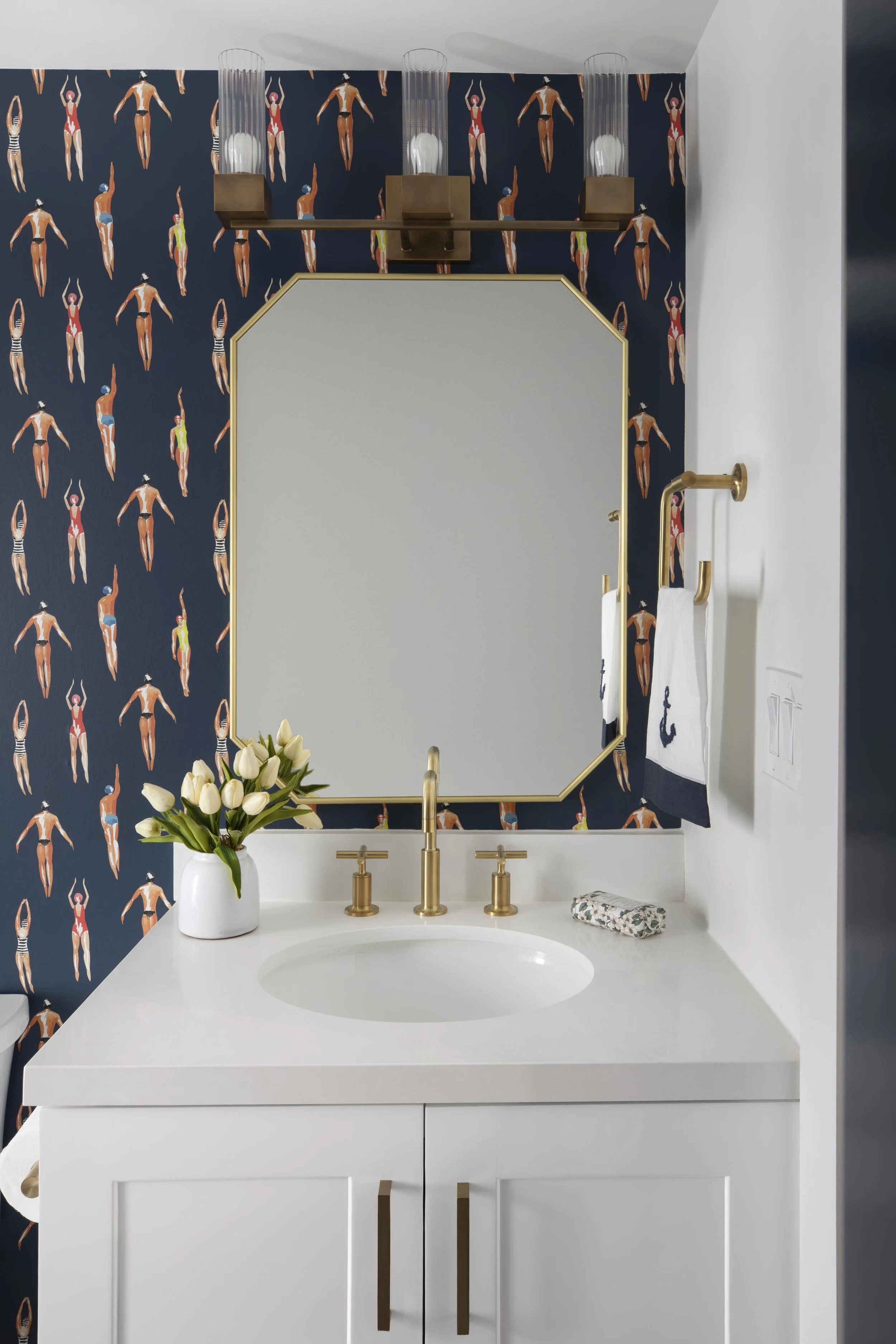 Bathroom vanity with swimmer wallpaper and brass fixtures