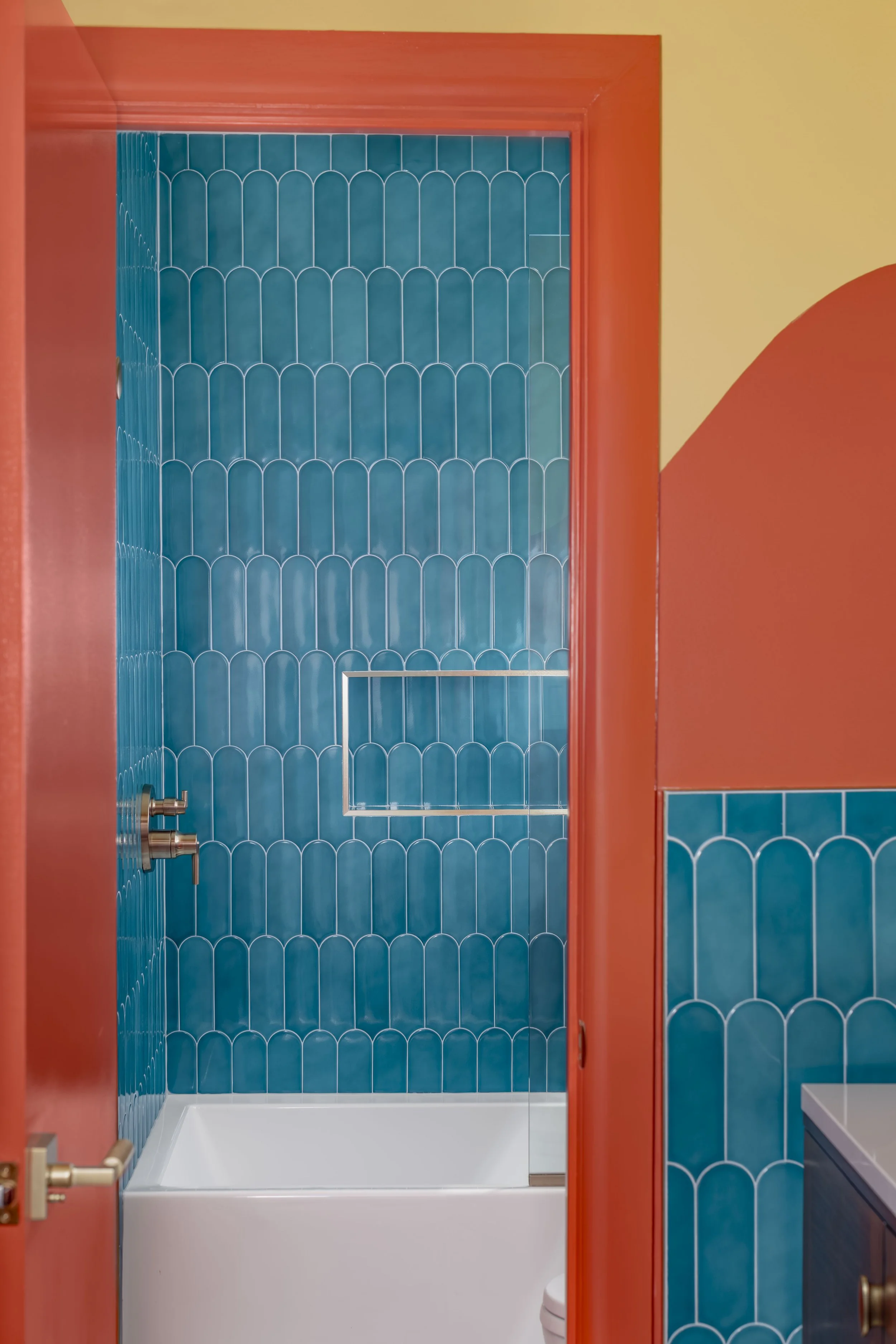 Tub surrounded by teal fish-scale tile seen through an orange door frame
