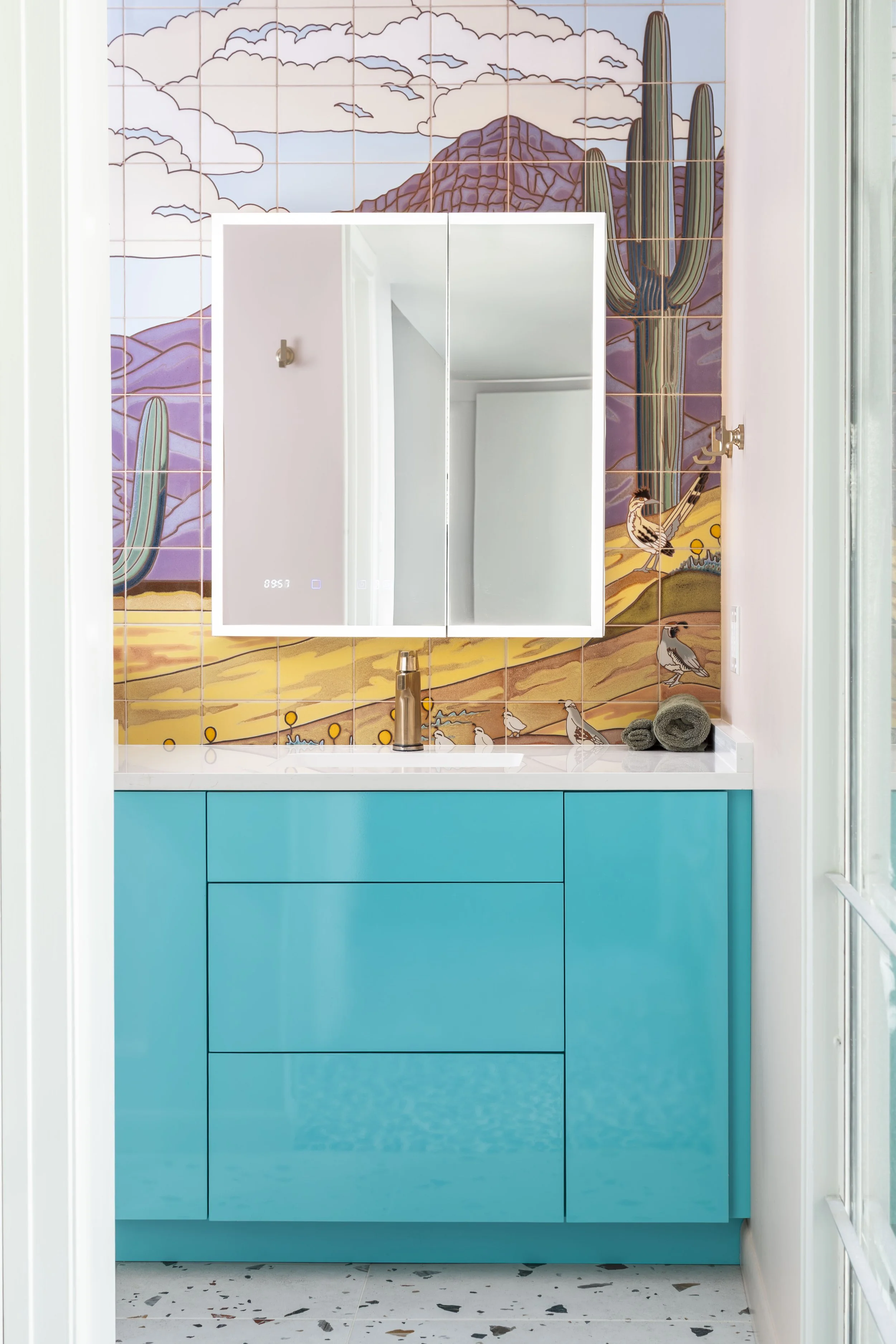 Turquoise vanity below a desert tile mural with roadrunner and quail