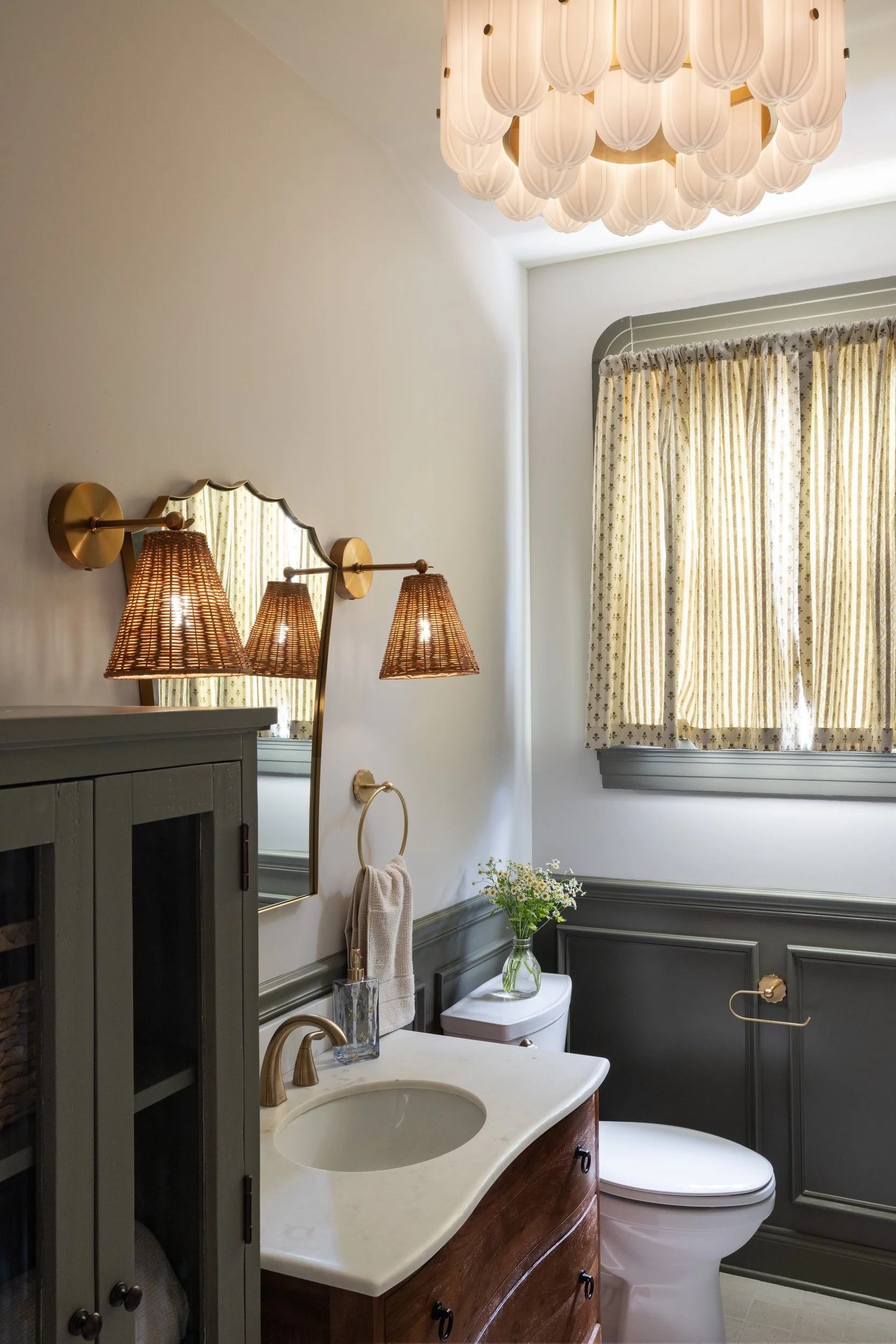 Bathroom with wicker sconces, scalloped mirror, and wood vanity under a glass flush mount