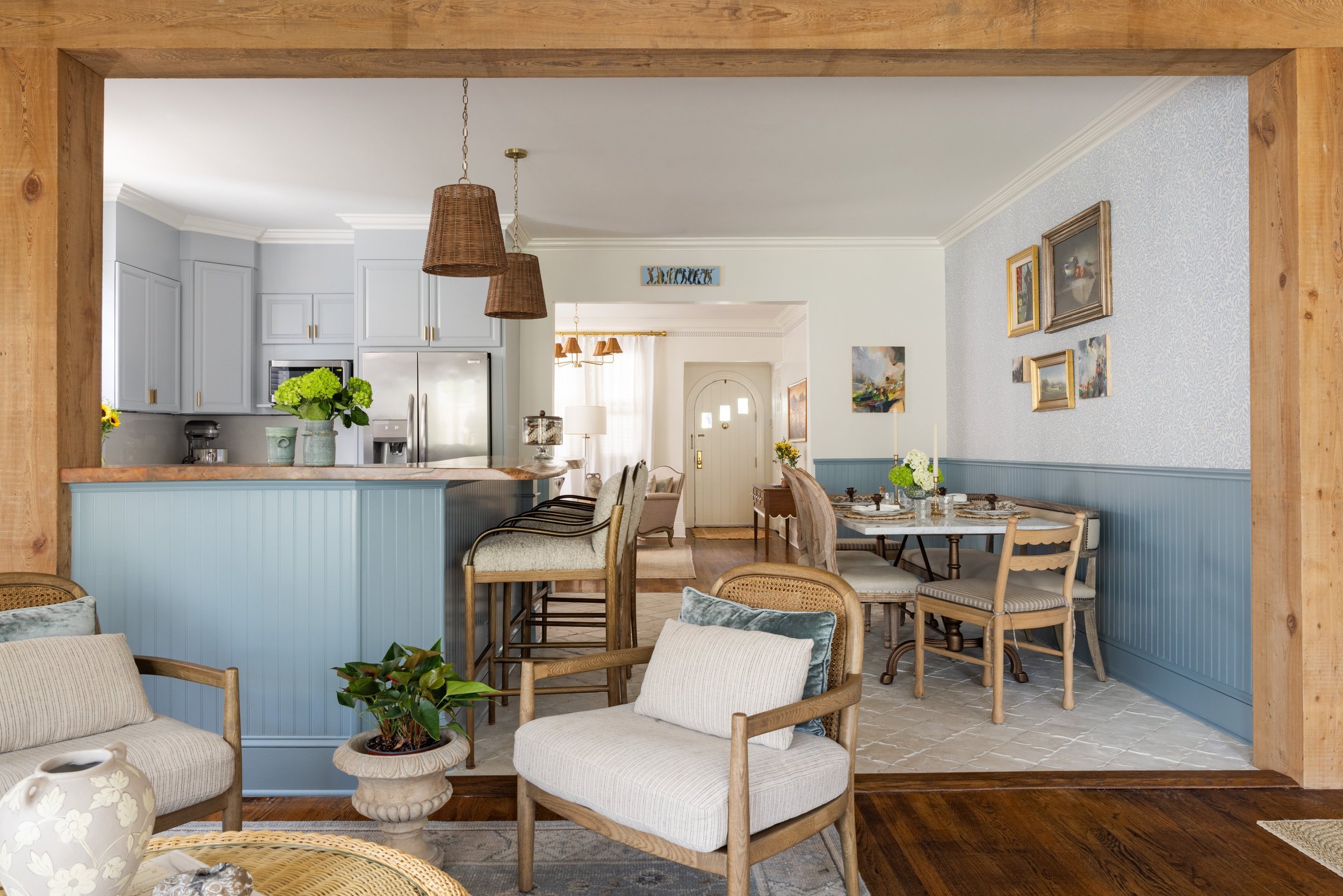 View through a reclaimed wood beam into a blue kitchen and wallpapered dining nook in Old Metairie