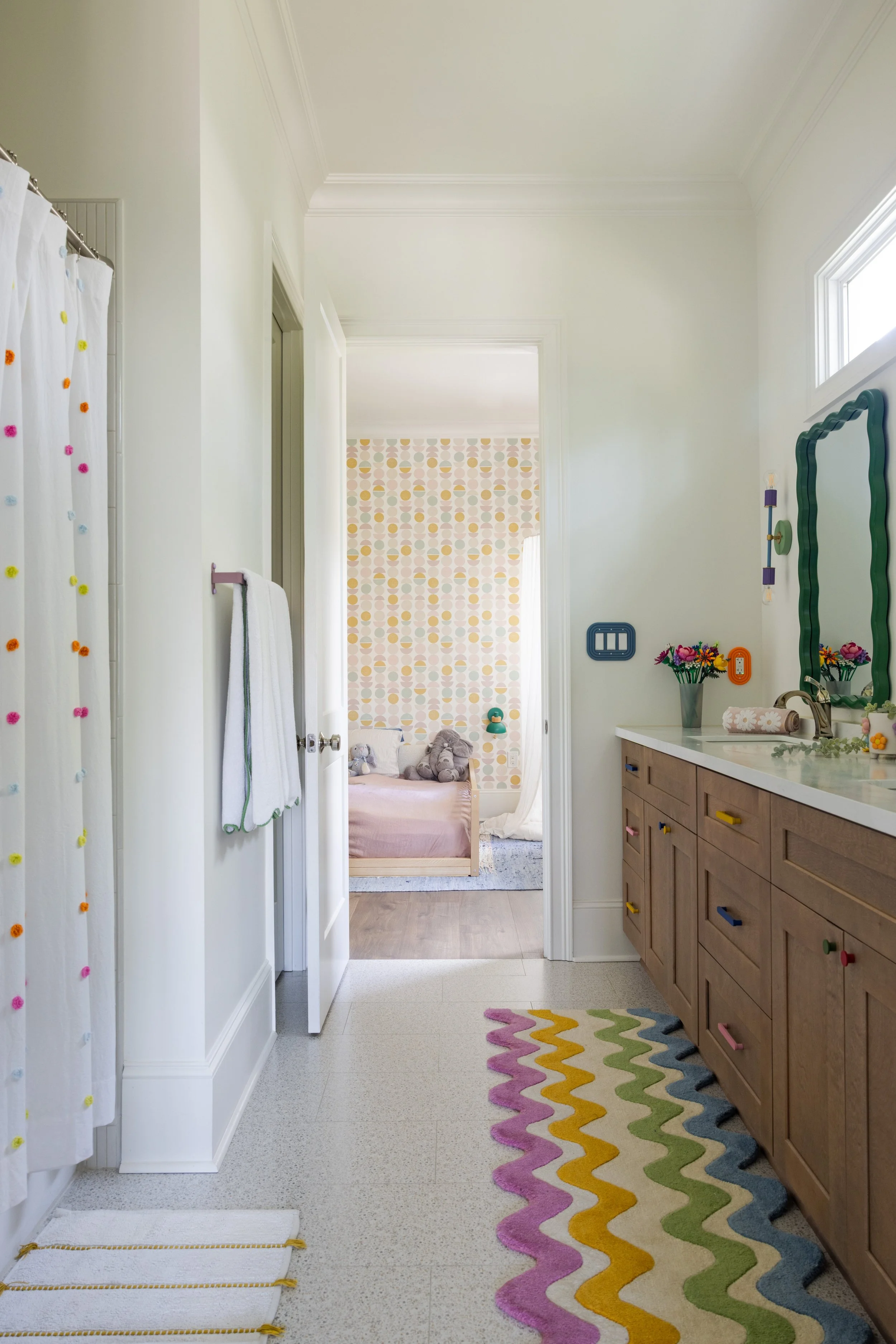 Kids' bathroom with wavy striped rug looking into a patterned bedroom